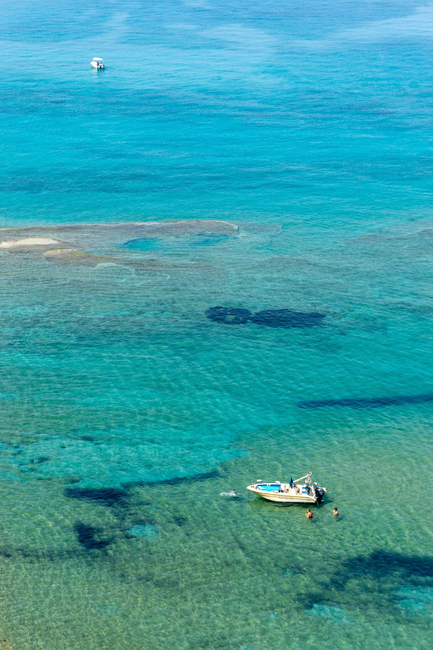 Aerial view of a small motorboat floating in clear turquoise Mediterranean sea water with visible rocky seabed. Corfu, Greece.