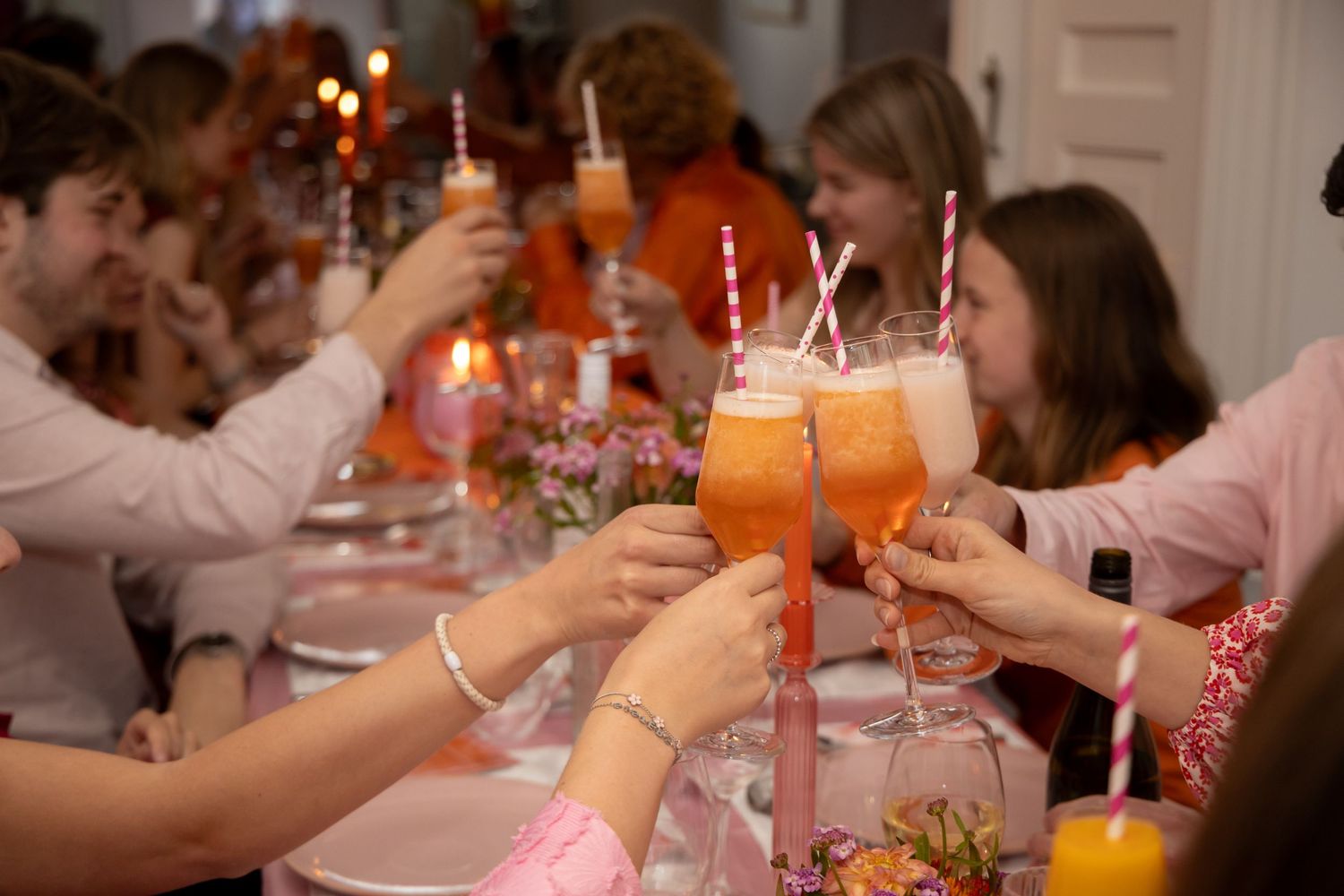 Friends toasting with orange cocktails and striped straws at festive dinner party.
Evelijn - 21 Diner - Event shoot