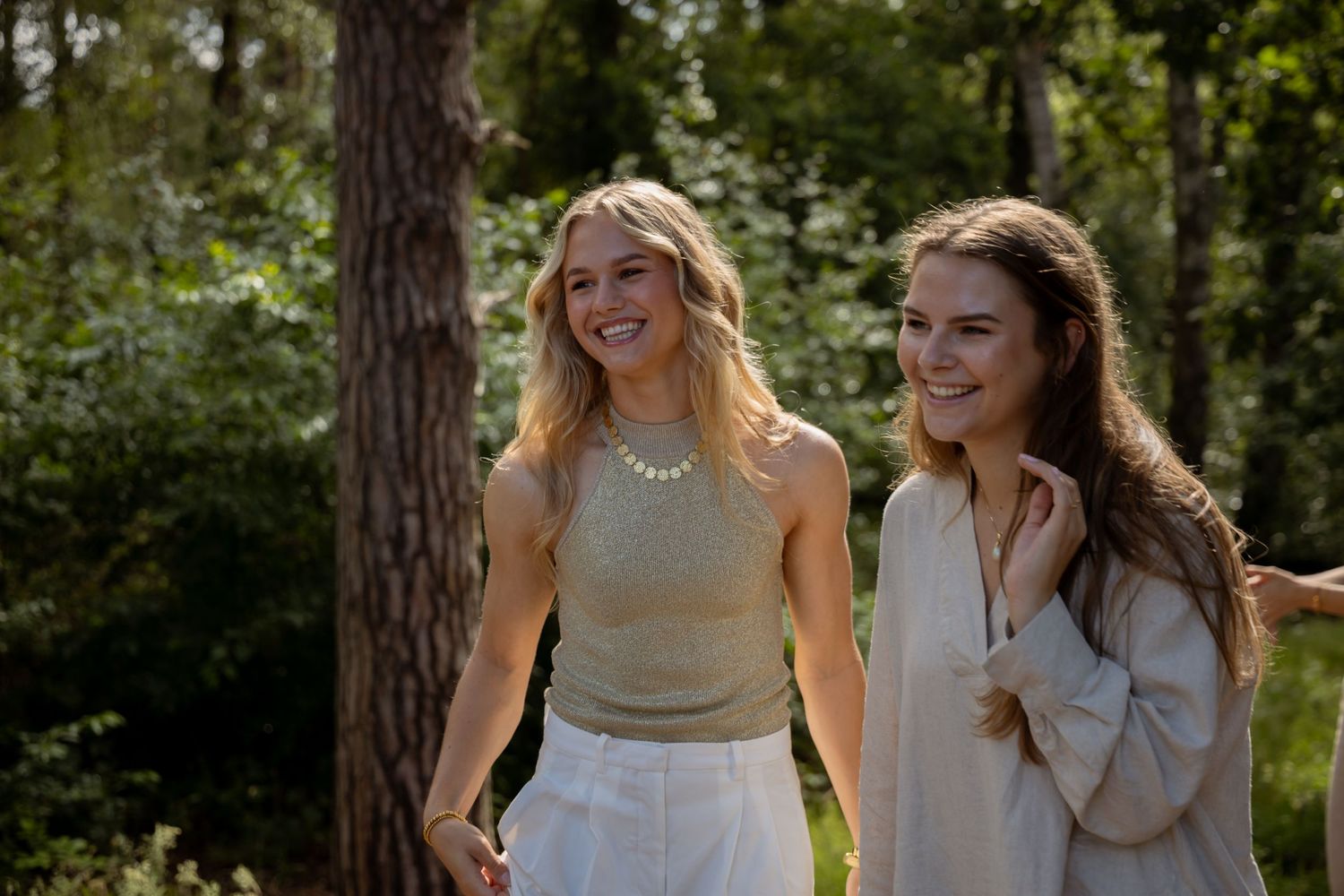 Two smiling young women walking outdoors among green trees on a sunny day, wearing casual summer outfits.
Familie Wormgoor - Familieshoot