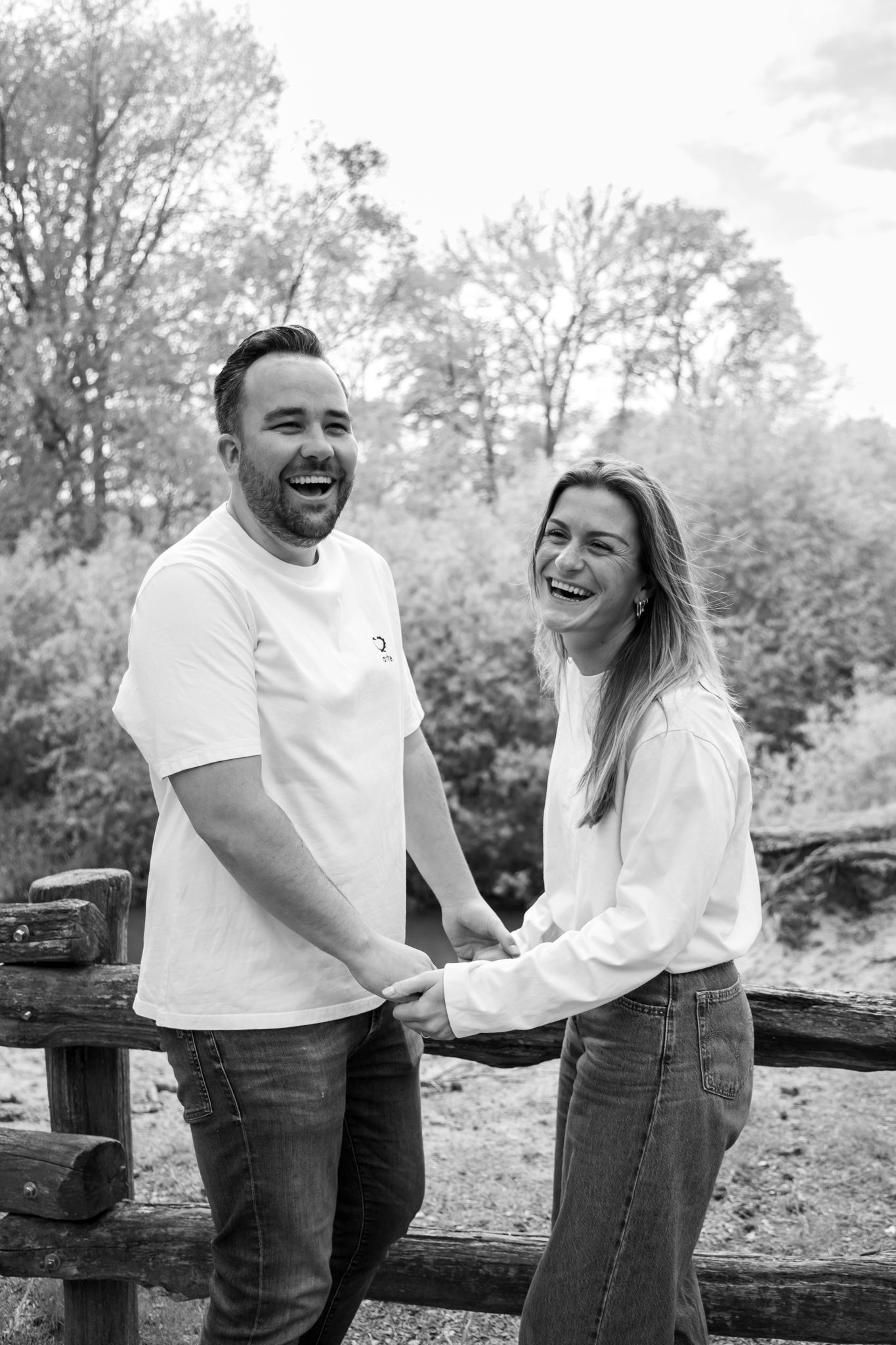 Black and white photo of laughing couple holding hands by wooden fence outdoors.
Fleur en Timo - Koppelshoot