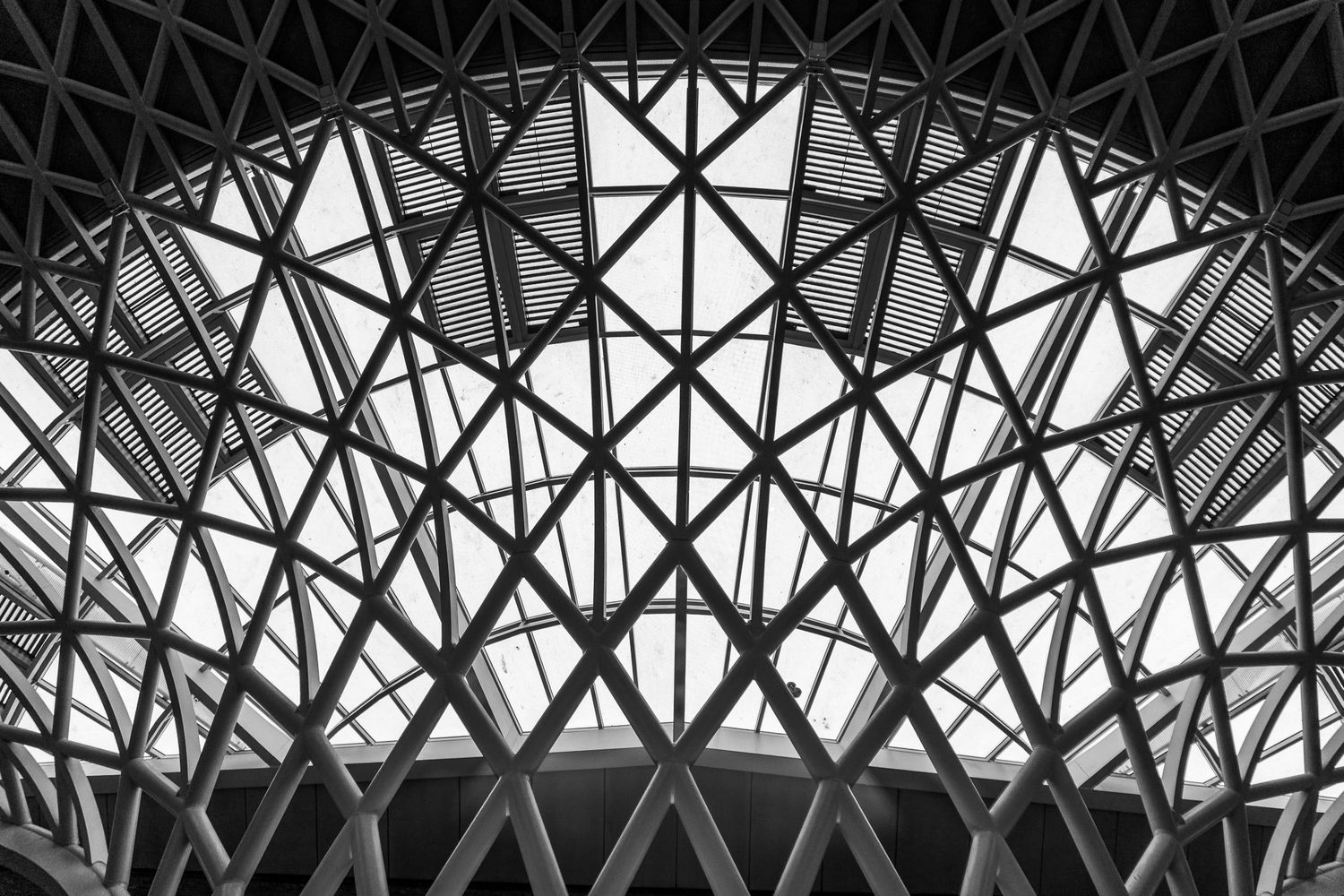 Black and white architectural photo of a geometric dome ceiling with intricate steel lattice framework and triangular patterns.
Londen, UK