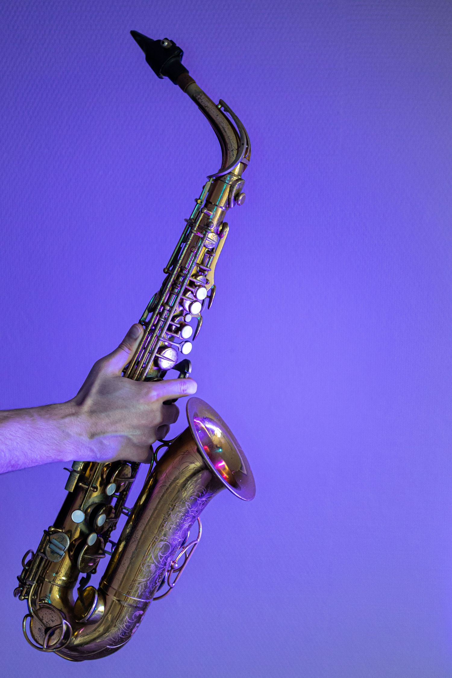 A hand holds a golden alto saxophone against a vibrant purple background under dramatic neon lighting.