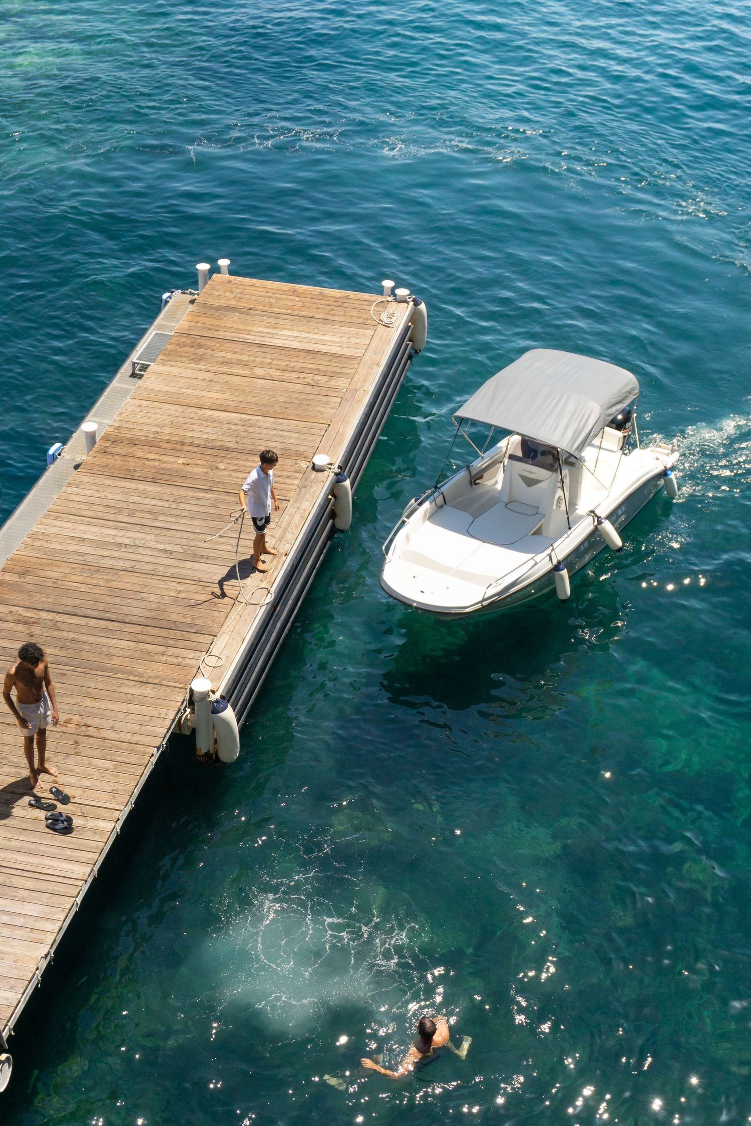 Aerial view of a wooden dock with a white motorboat, two people standing, and a swimmer in turquoise water.
Reizen - Lynn - Amalfi