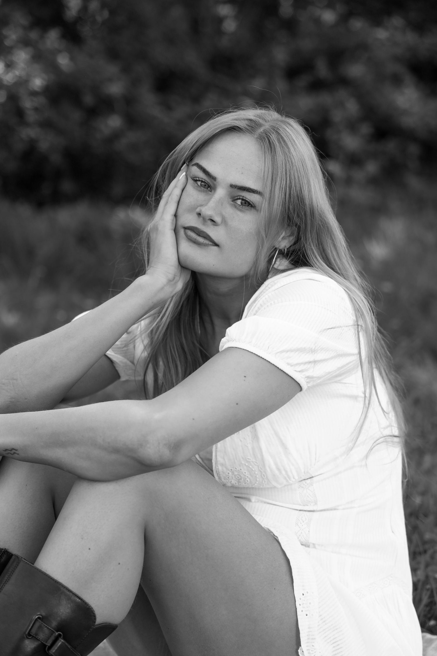 Black and white portrait of a blonde woman in a white dress sitting outdoors, resting her hand on her face.
Romy - Soloshoot