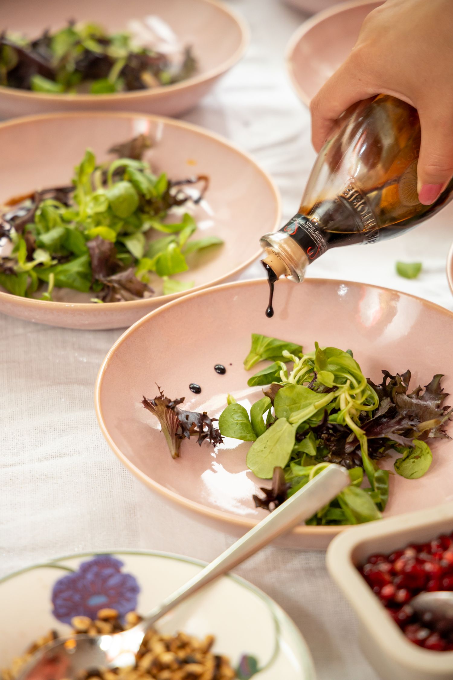 Dark balsamic dressing being poured from a bottle onto fresh green salad in pink ceramic bowls.
Evelijn - 21 Diner - Event shoot