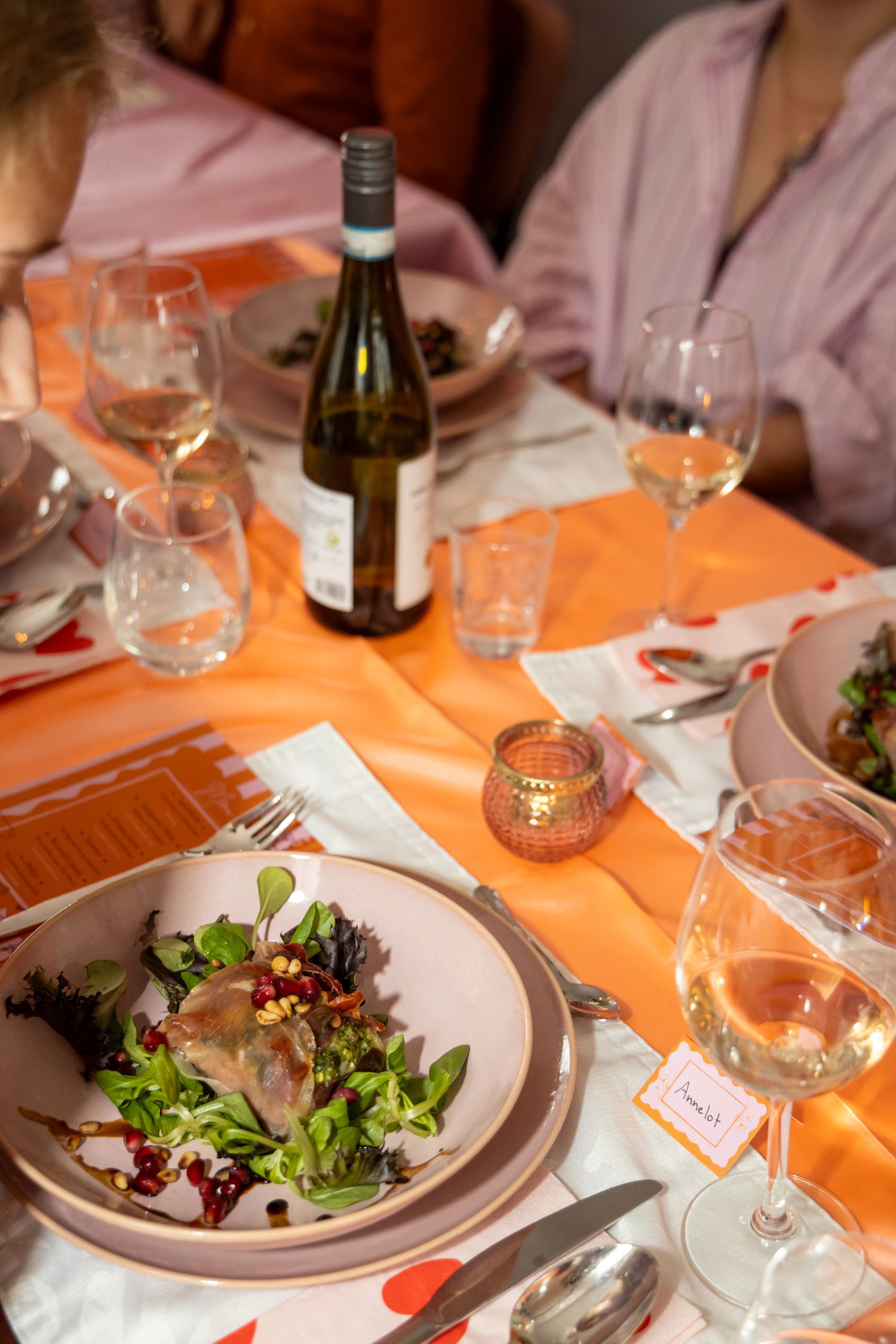Elegant dinner table with fresh green salad, wine glasses, and a bottle of white wine on an orange tablecloth.
Evelijn - 21 Diner - Event