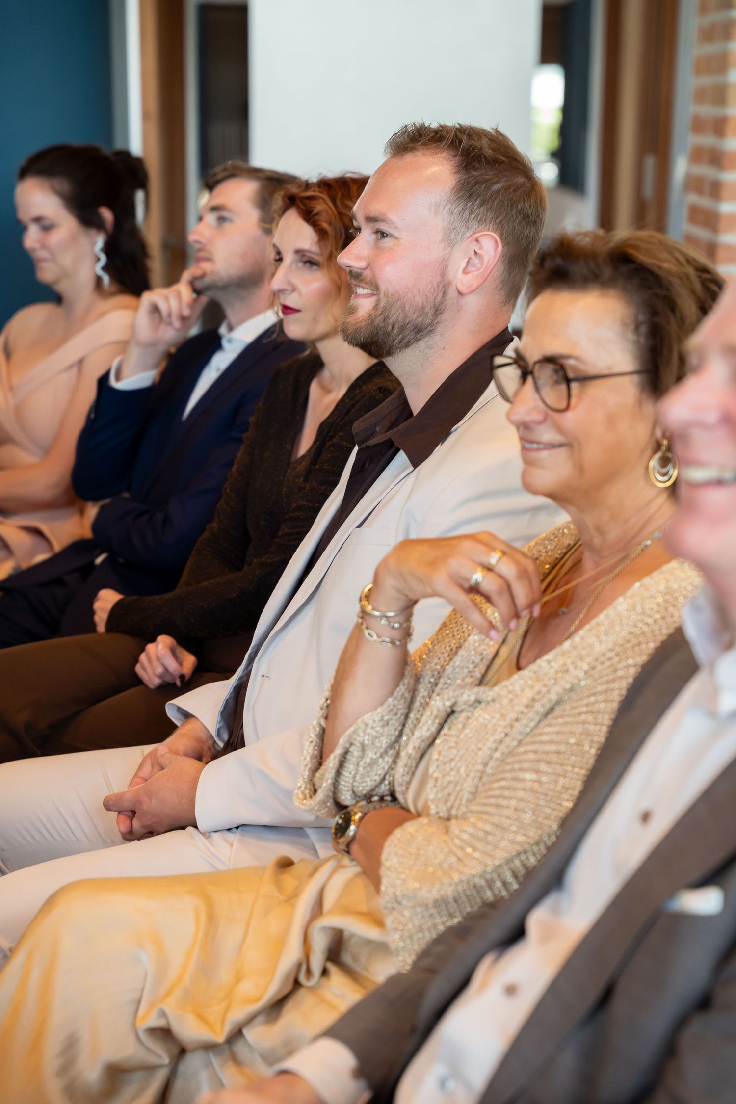 Audience members smiling and engaged during a wedding ceremony, seated in rows in a modern room.