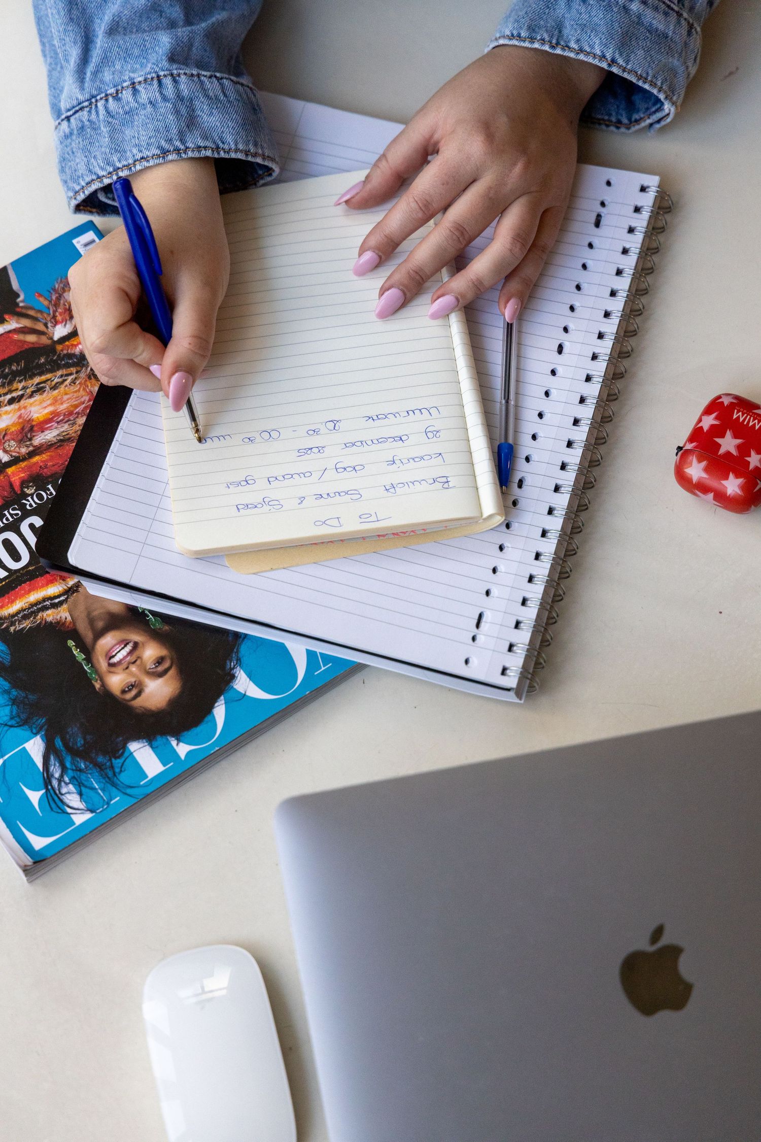 Overhead view of hands writing in notebook beside Apple laptop, magazine, and mouse on white desk.
Emma - Reefolution - Brandingshoot