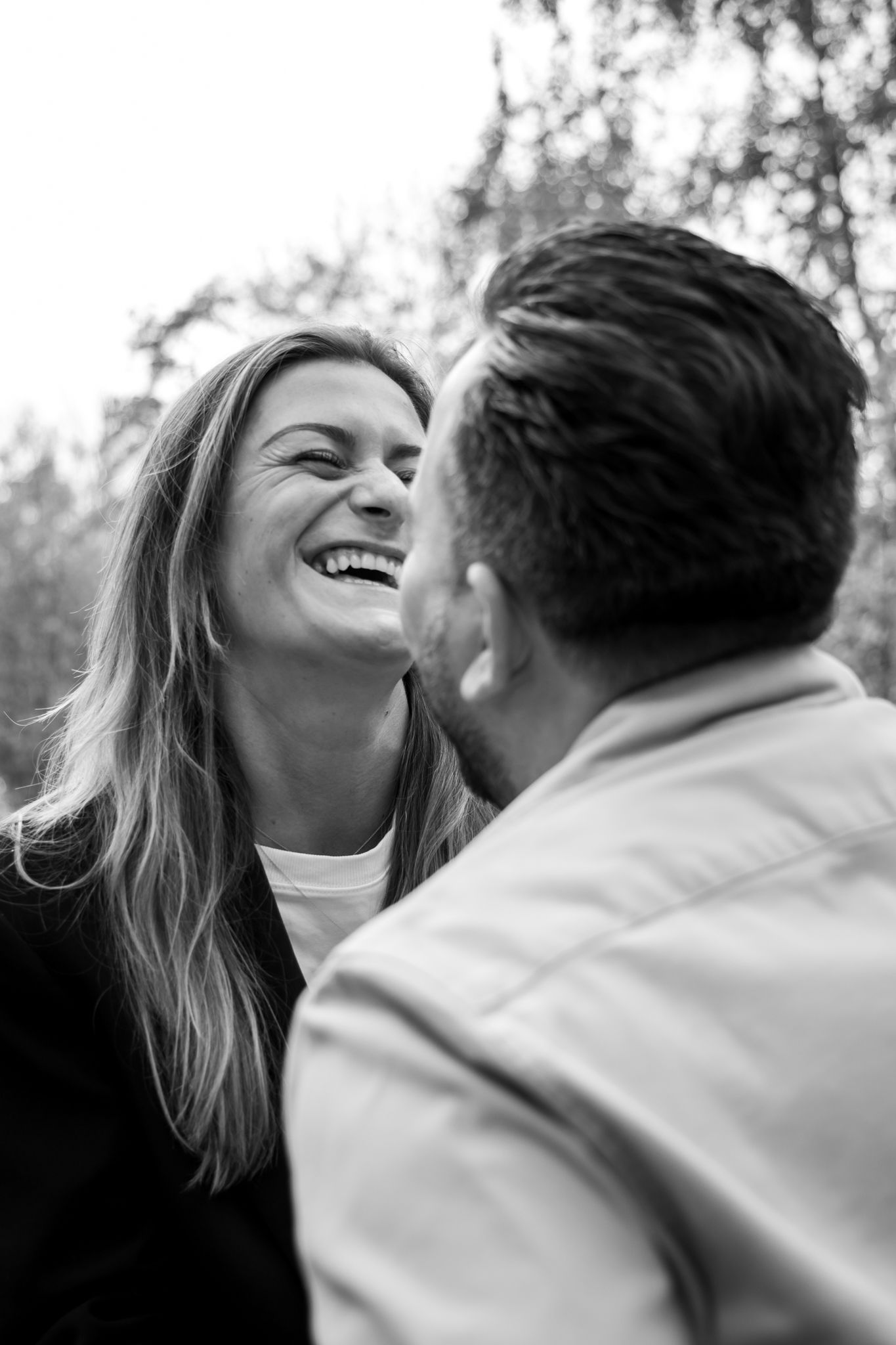 Black and white photo of a laughing woman and man sharing a joyful moment outdoors among trees.
Fleur en Timo - Koppelshoot