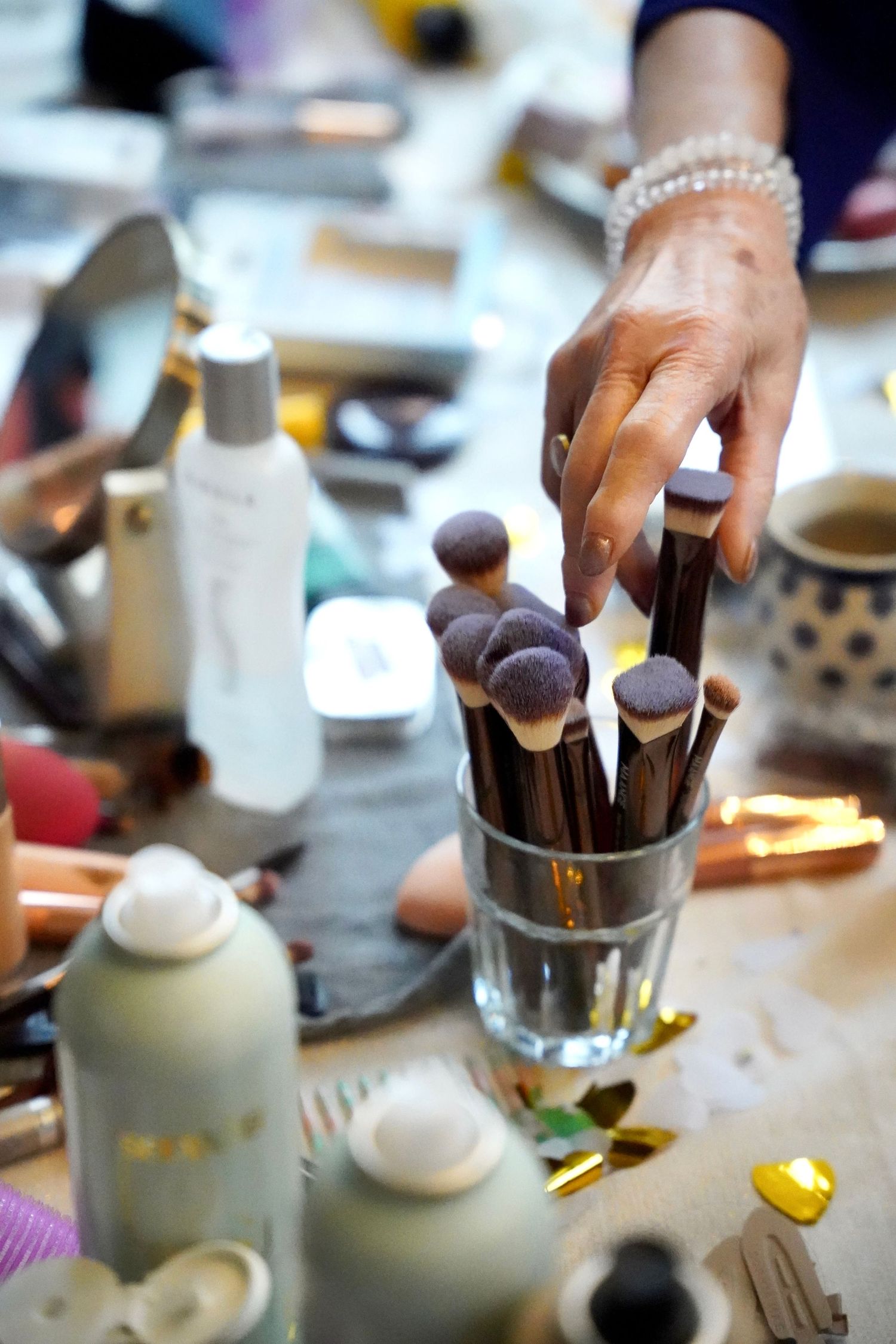 A hand reaching for makeup brushes with purple tips in a glass, surrounded by beauty products on a vanity table.
Sjoerd en Sanne - Bruiloft