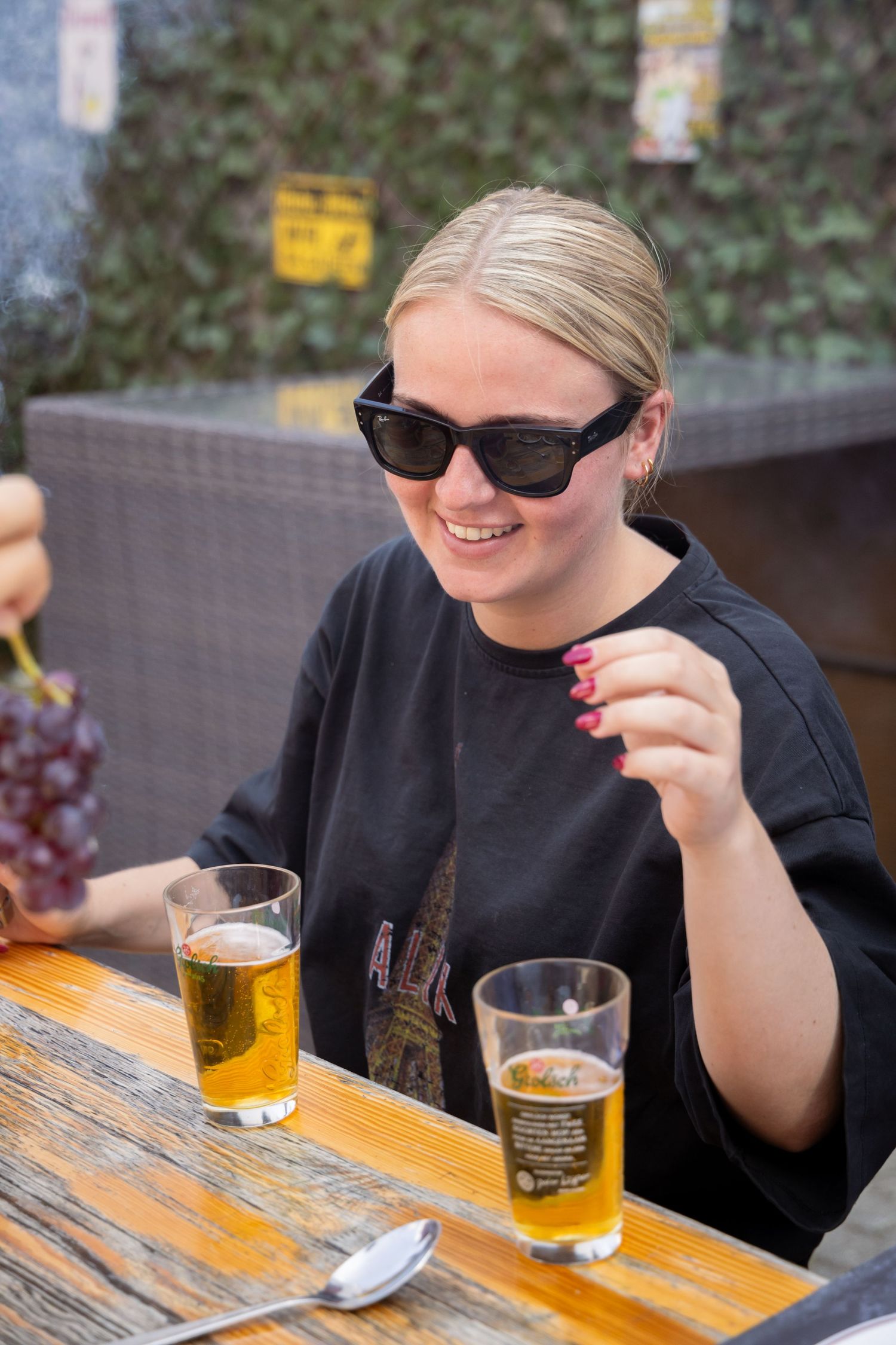 Smiling blonde woman in sunglasses enjoying beer and grapes at an outdoor table.
Yips - BBQ - Brandingshoot