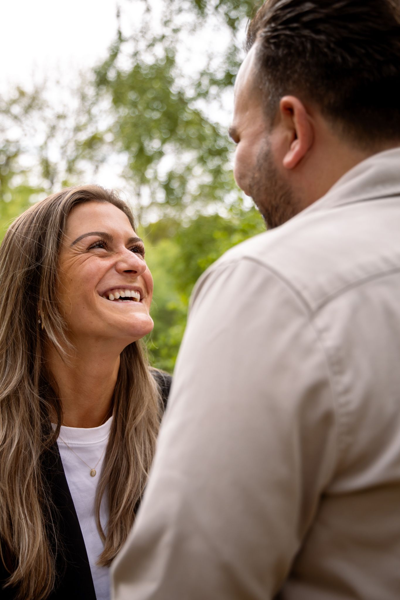 A smiling woman with long hair gazes happily at a man outdoors, surrounded by lush green trees.
Fleur en Timo - Koppelshoot