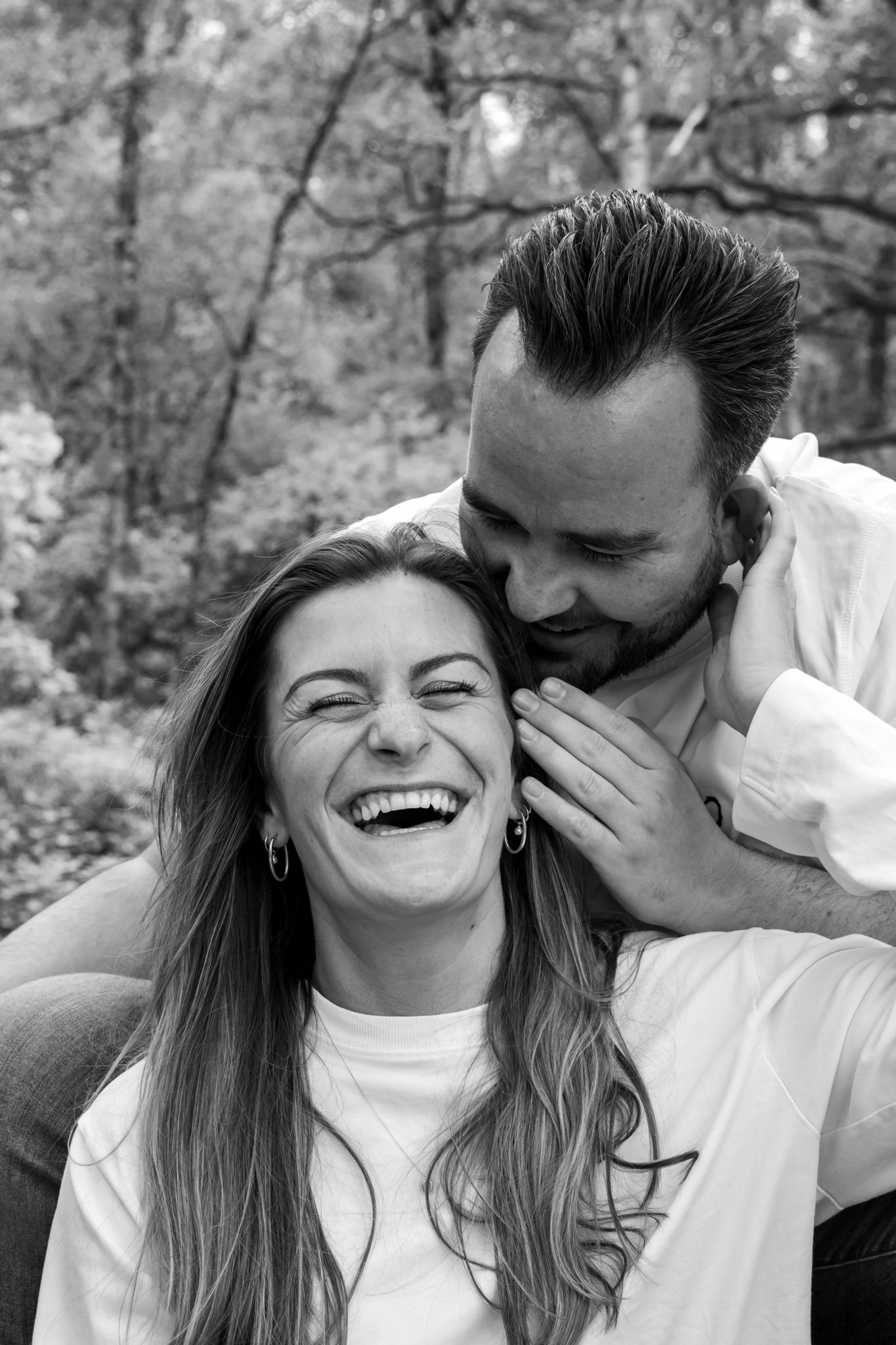 Black and white photo of a laughing woman and smiling man sharing a joyful moment outdoors in a forest setting.
Fleur en Timo - Koppelshoot