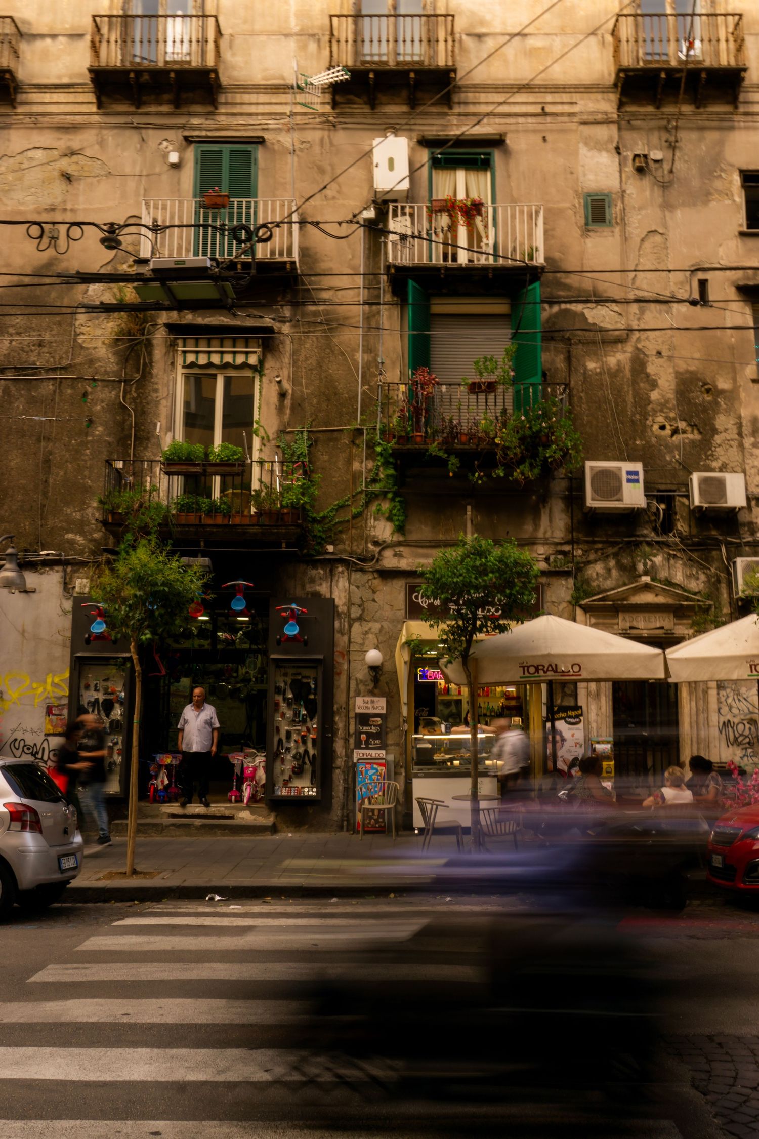 Weathered Italian street building with green balconies, shops, and motion-blurred traffic on a busy urban intersection.
Lynn - Napoli