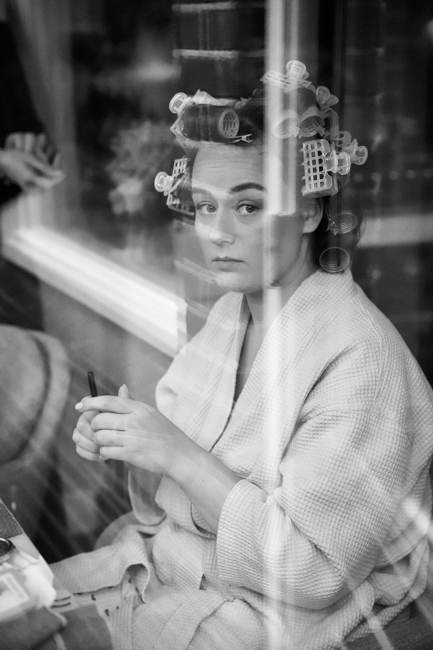 Black and white photo of a woman in a robe with hair rollers, shot through a window.
Sjoerd en Sanne - Bruiloft - Klaarmaken