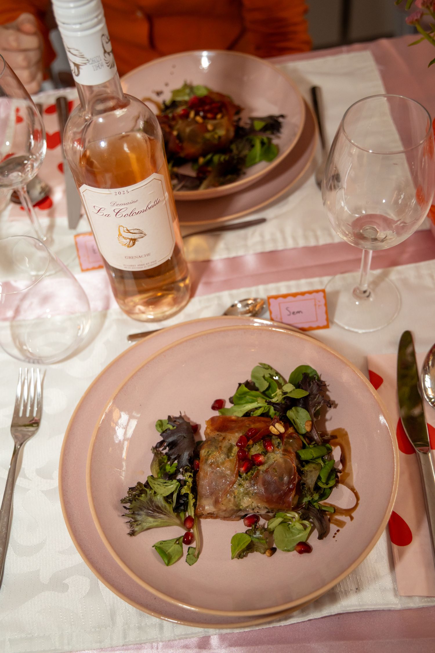 Elegant plated main course with greens and pomegranate seeds beside a rosé wine bottle on a pink table.
Evelijn - 21 Diner - Event shoot
