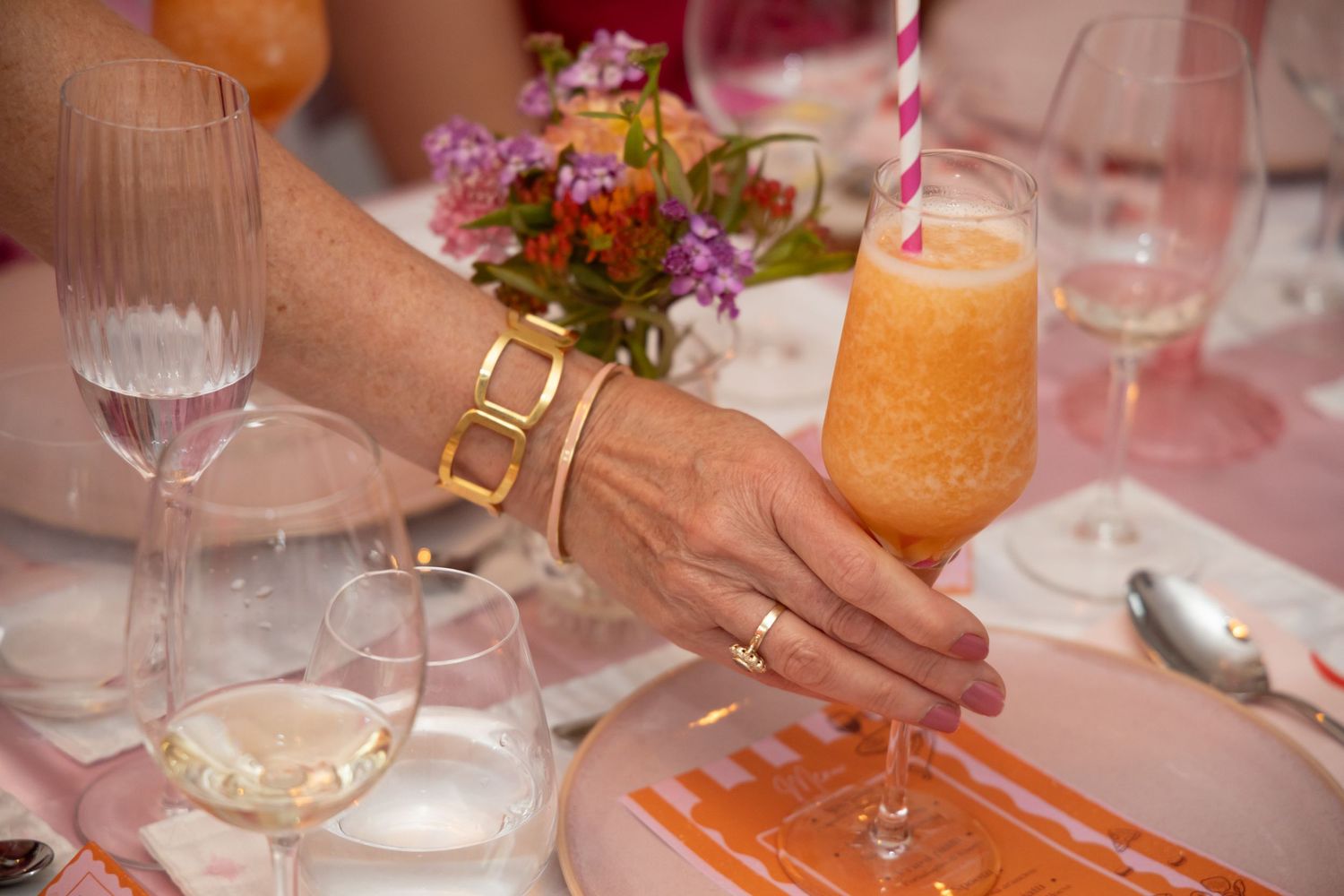 Woman with gold bracelet holding an orange cocktail with a striped straw at a dinner.
Evelijn - 21 Diner - Event shoot