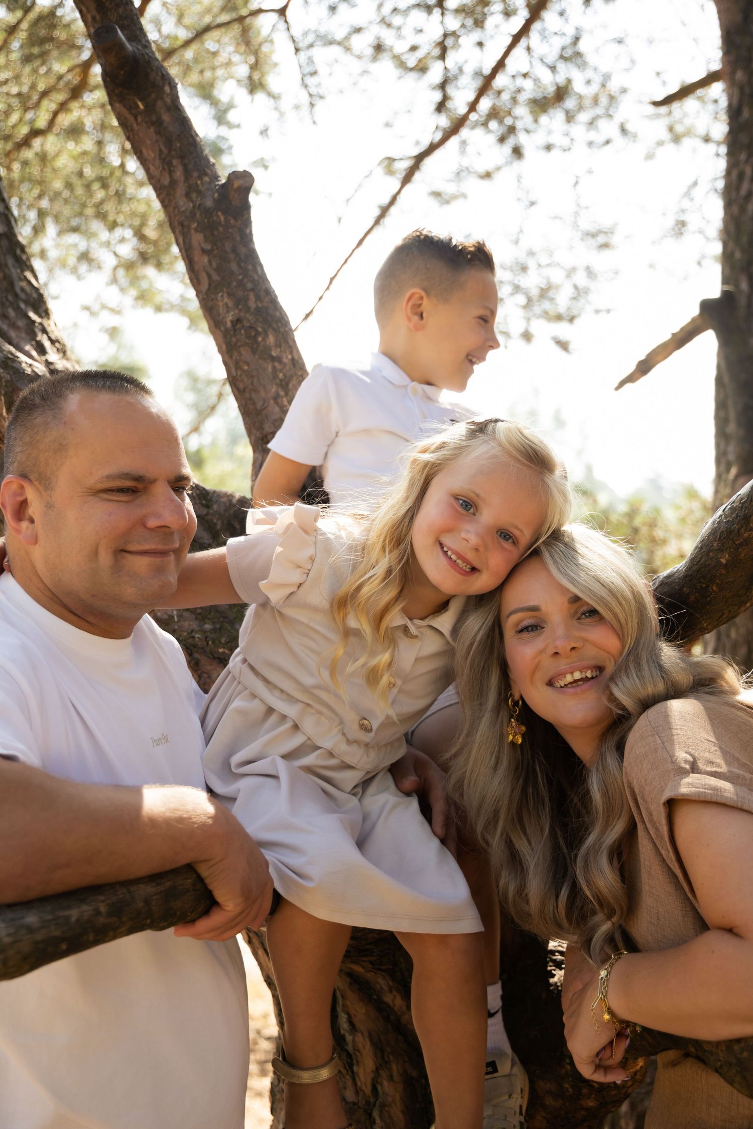 Happy family of four posing outdoors among trees, with two parents and children smiling in a sunny forest setting.
Familieshoot