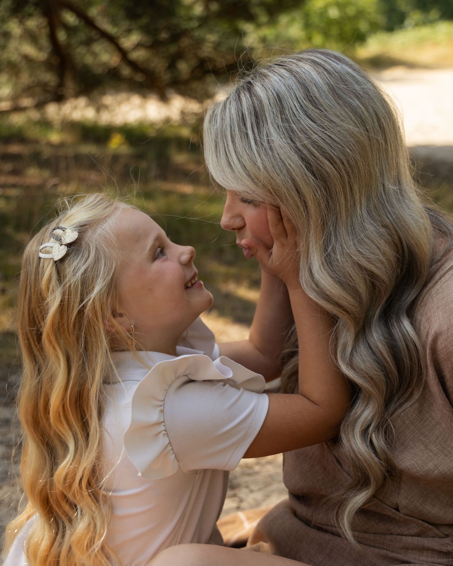A mother and young daughter with long blonde hair share a sweet moment outdoors, gazing at each other lovingly.
Familieshoot