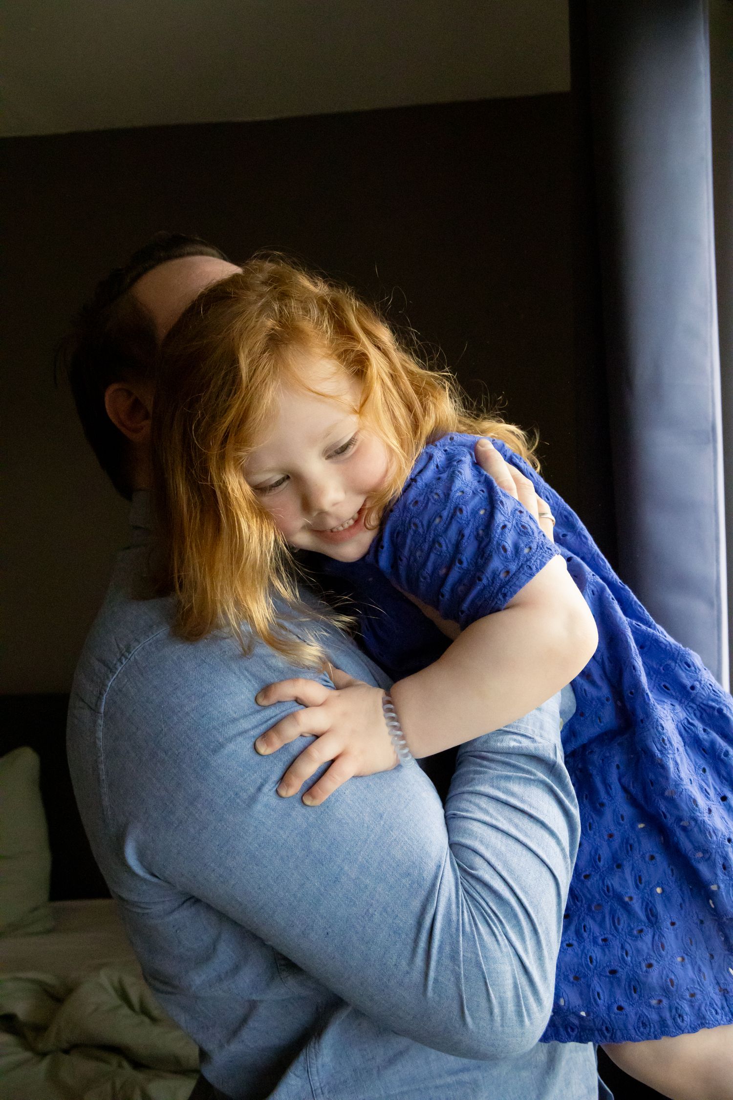 Happy girl in blue dress hugging adult in warm embrace by window.
Ellis - Newborn shoot