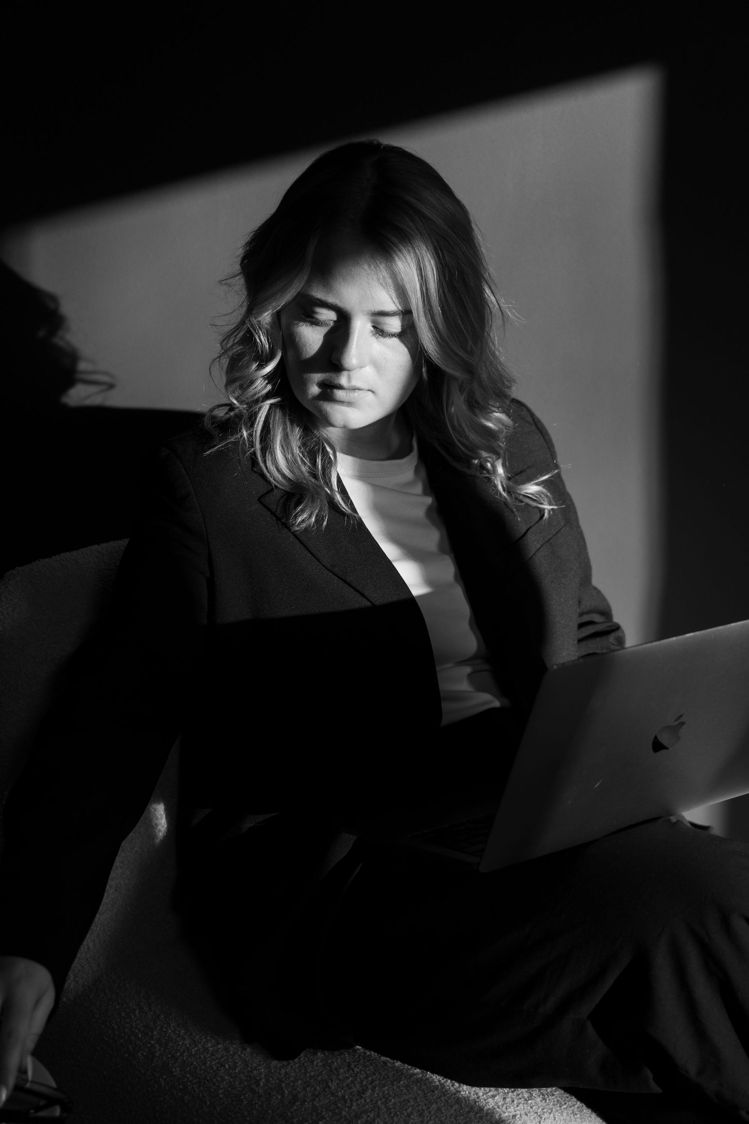 Black and white photo of a woman in a blazer working on a laptop in dramatic chiaroscuro lighting.
Emma - Reefolution - Brandingshoot