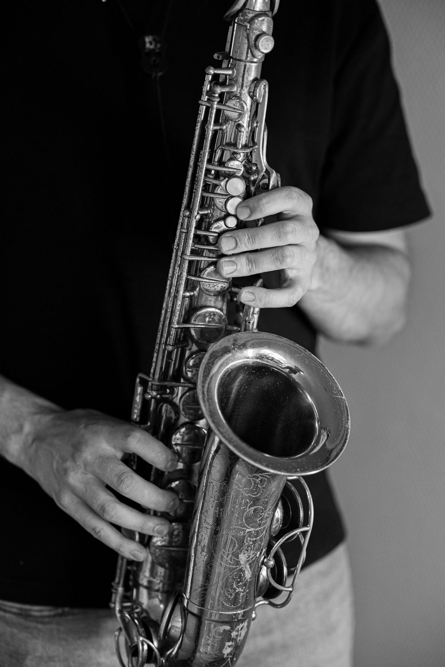 Black and white photo of a musician playing a vintage alto saxophone, hands visible on keys.