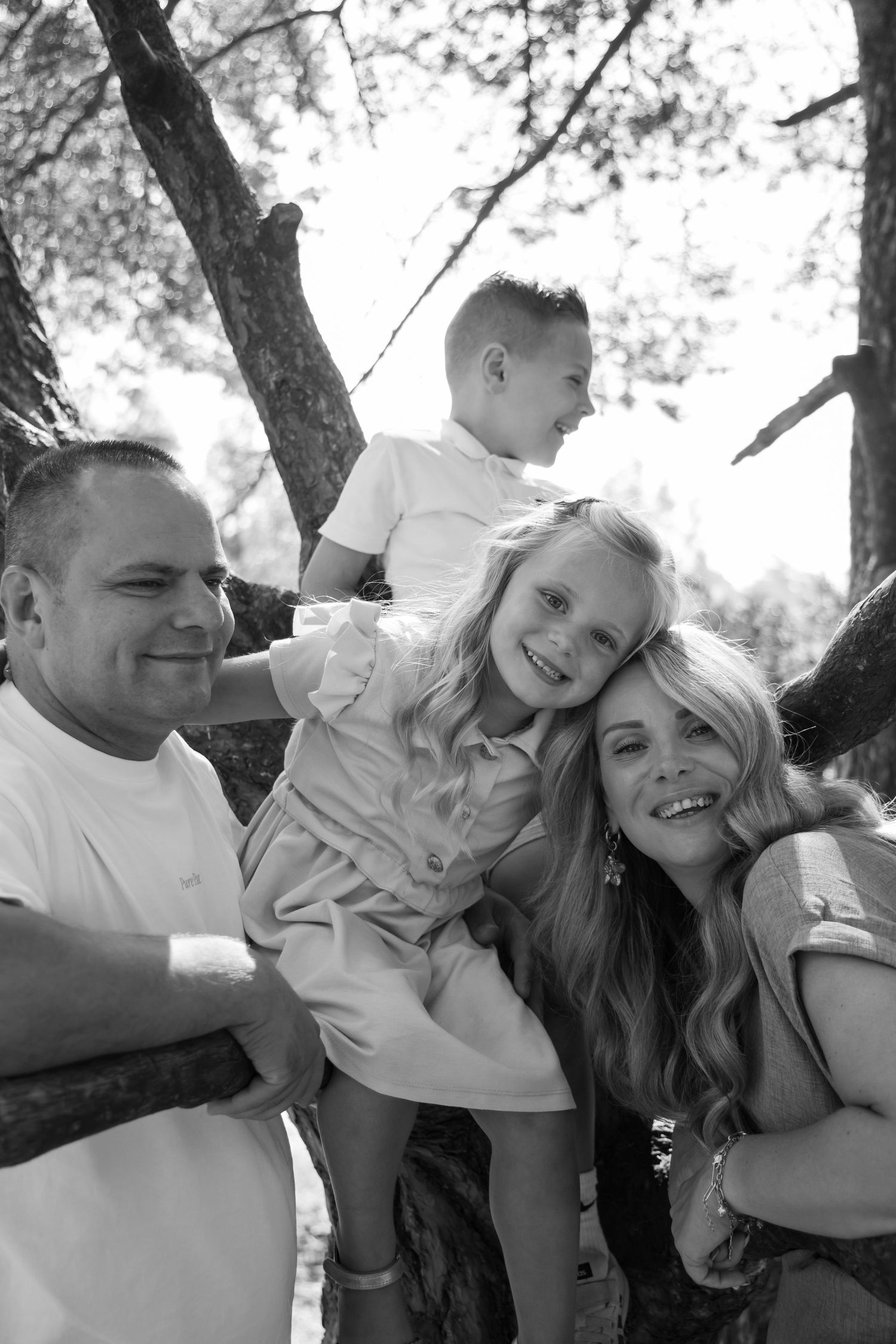 Black and white family portrait with parents and two children playing in a tree outdoors.
Familieshoot