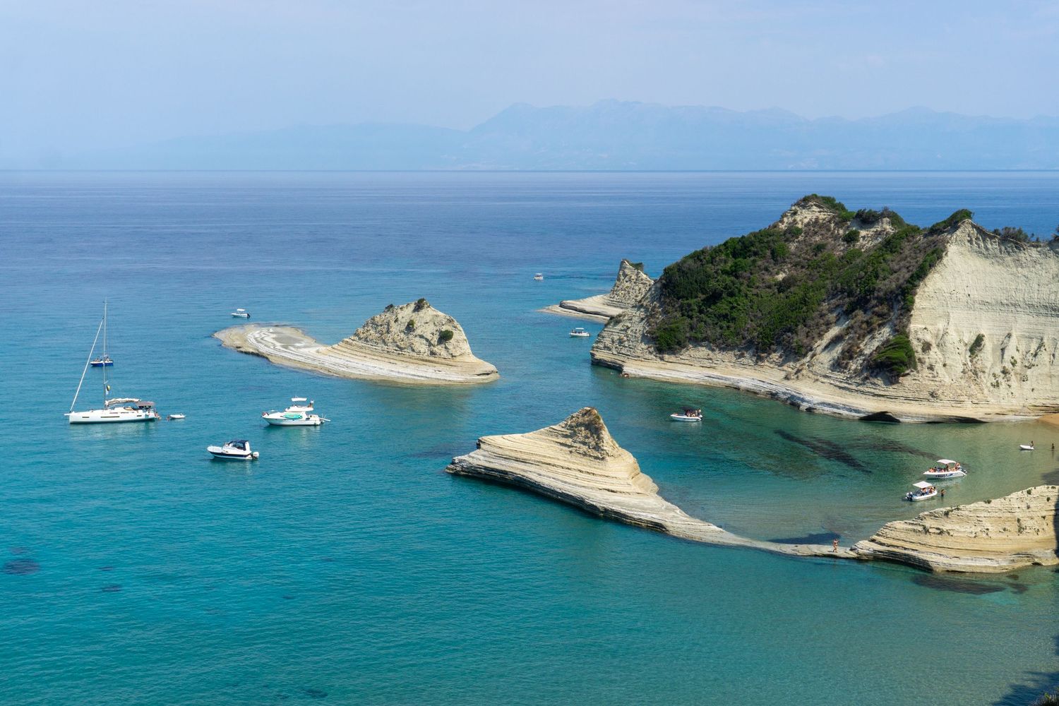 Aerial view of turquoise waters, white limestone cliffs, and sailboats near Cape Drastis, Corfu, Greece.