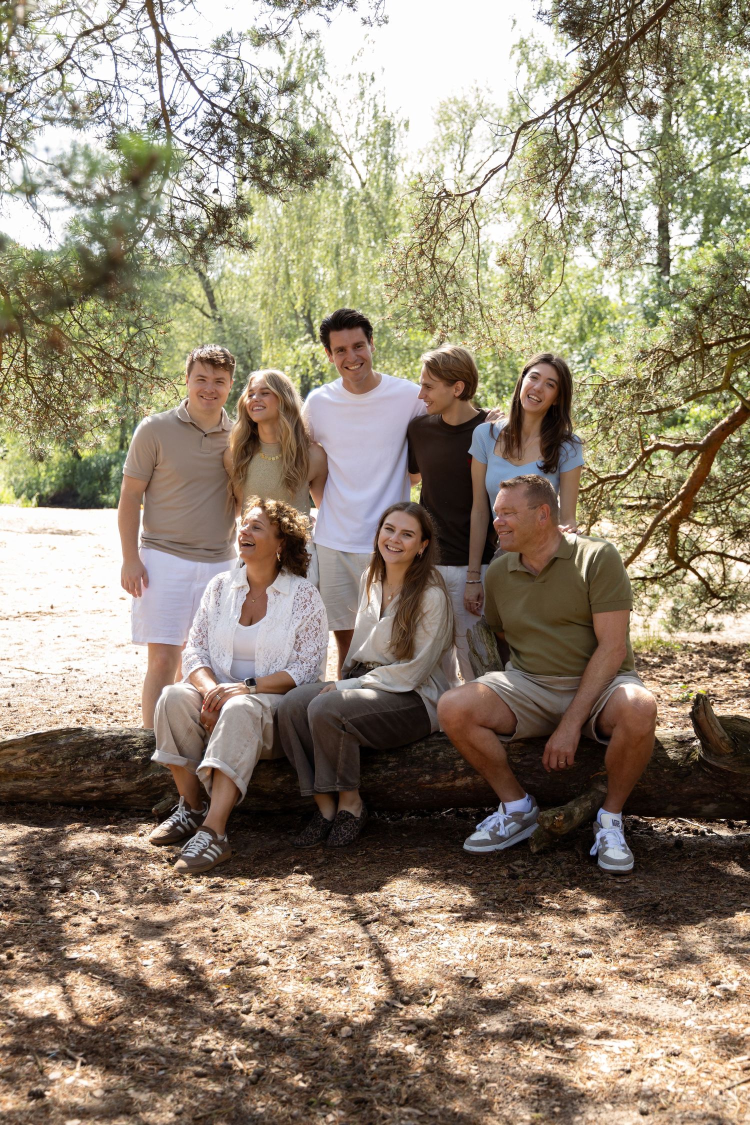 A happy family of eight poses together on a fallen log in a sunny pine forest setting.
Familie Wormgoor - Familieshoot