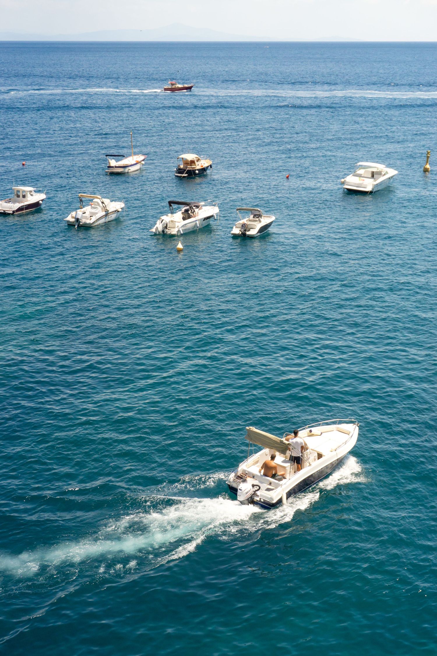 Aerial view of white motorboats anchored in turquoise Mediterranean waters, with one speedboat creating a wake.
Reizen - Lynn - Amalfi