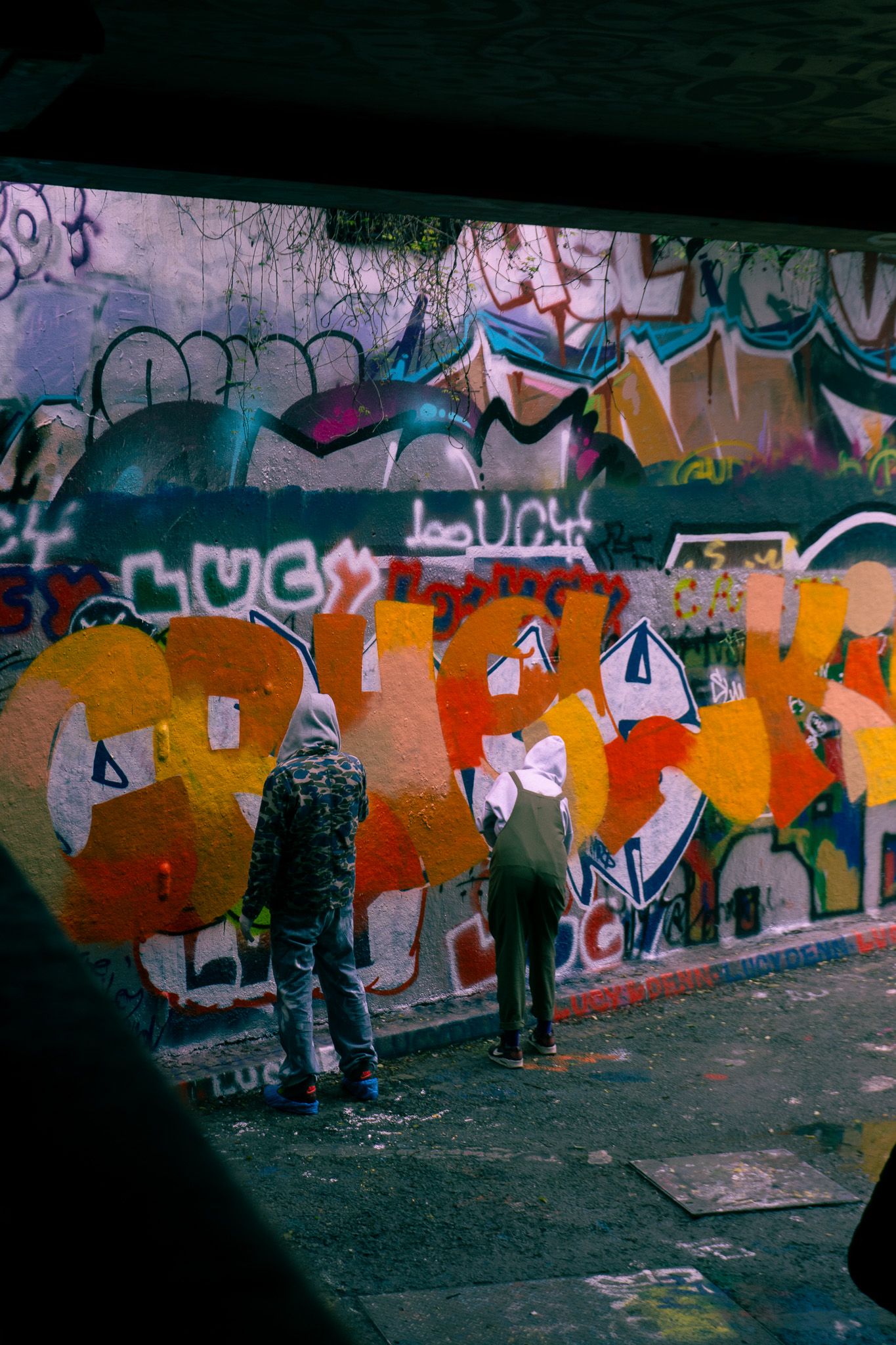 Two graffiti artists spray painting a colorful mural on an urban wall covered in vibrant street art at night.
Reizen - Lynn - Londen