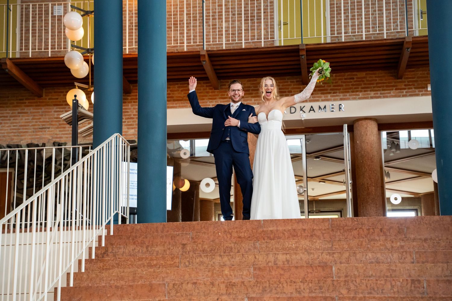 Joyful newlyweds celebrating on steps outside Kramer venue, bride holding bouquet in white gown, groom in navy suit.