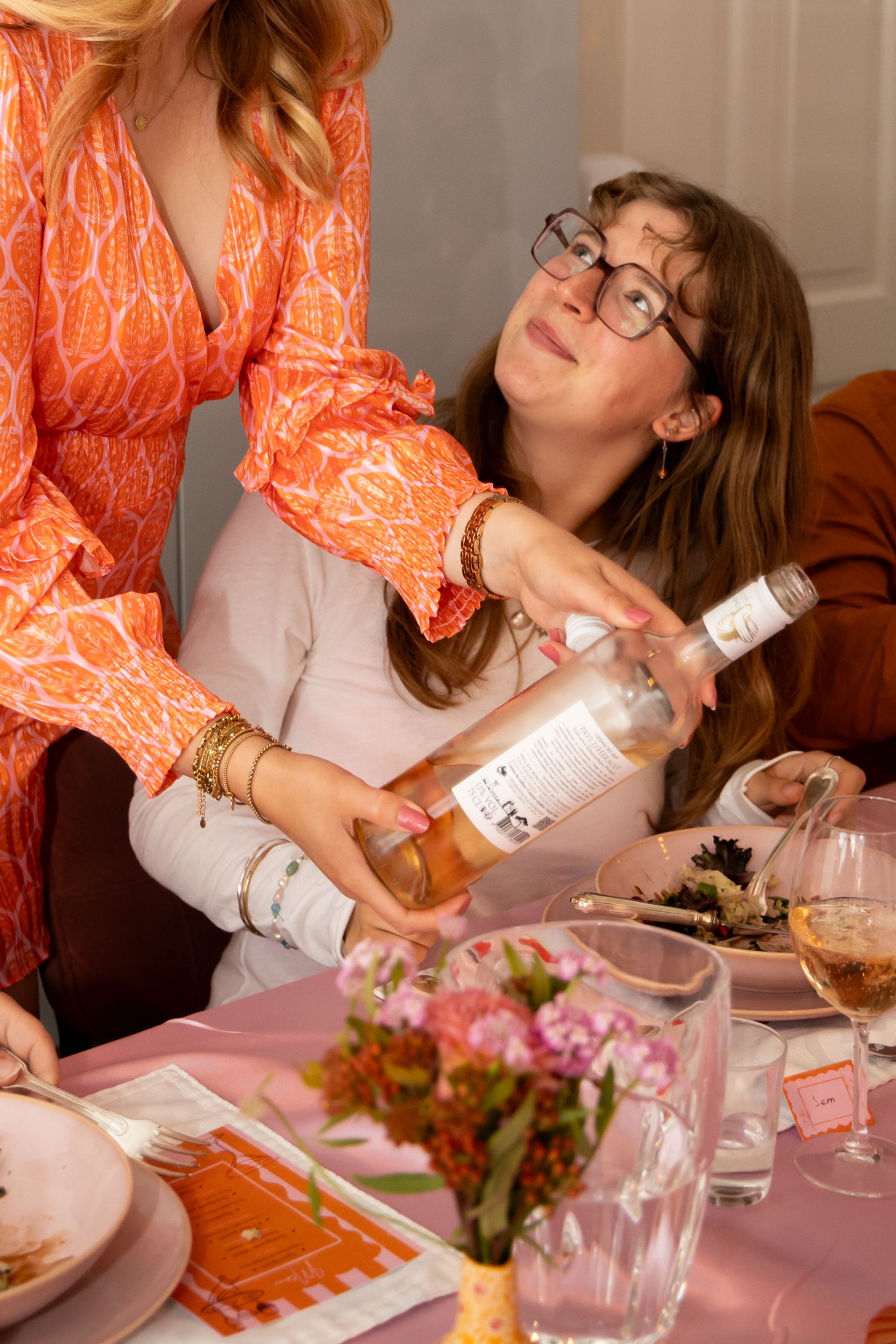 Woman in orange dress pouring rose wine for a guest at a pink dinner party.
Evelijn - 21 Diner - Event shoot