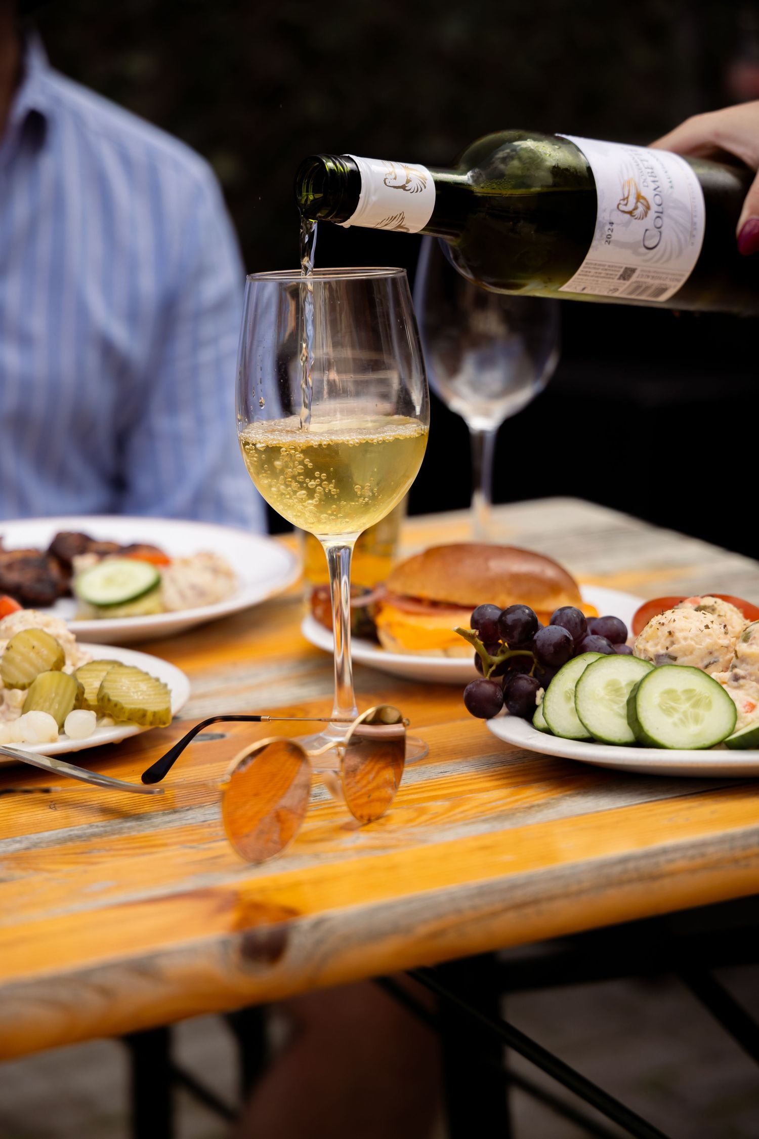 White wine being poured into a glass at an outdoor dining table with fresh vegetables, grapes, and food platters.
Yips - BBQ - Brandingshoot