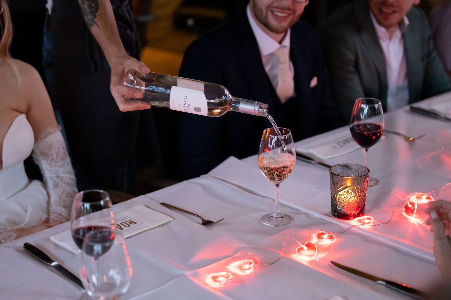 Wine being poured into a glass at an elegant wedding reception dinner table with glowing red candles.