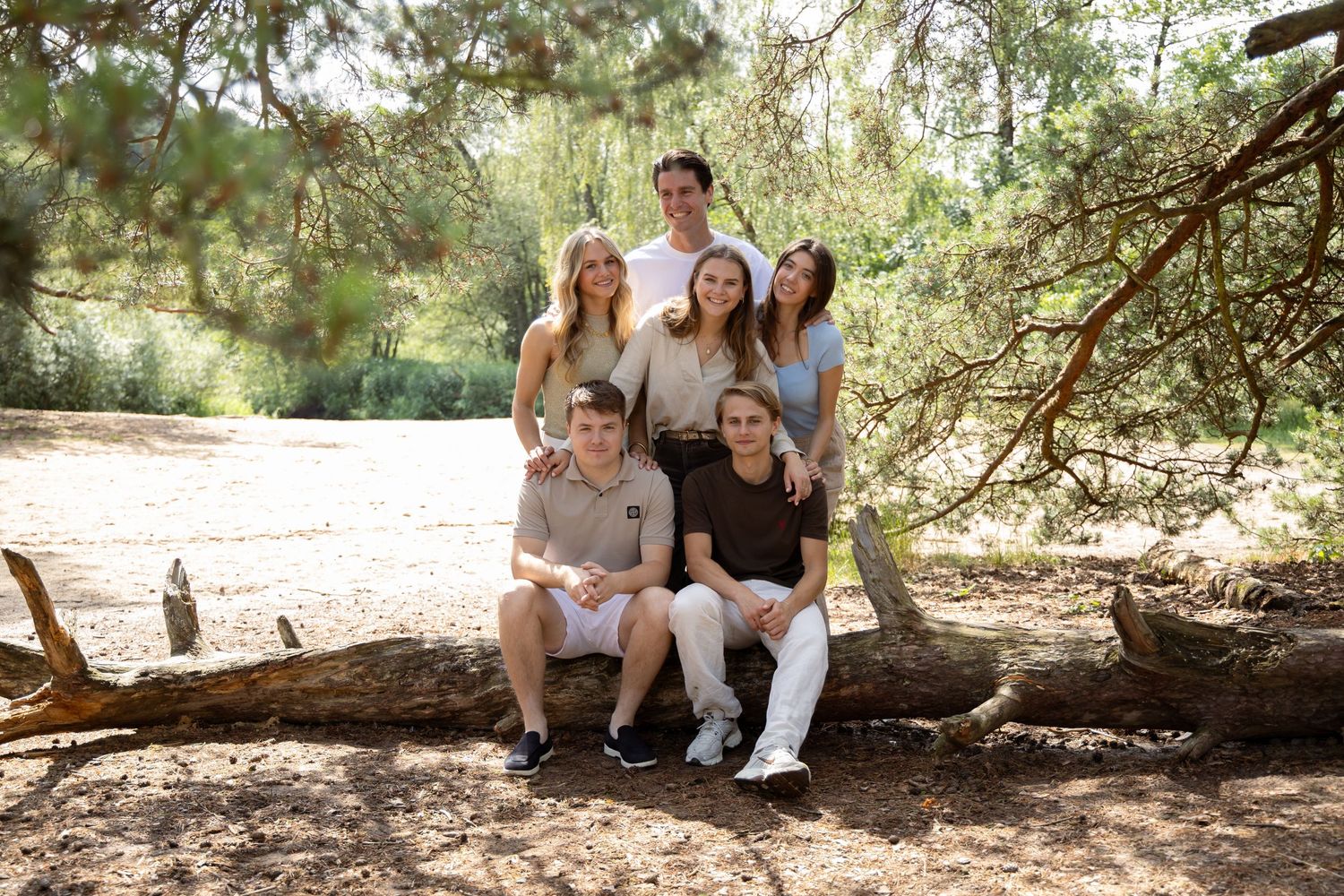 Group of six young adults posing together on a fallen log in a sunny pine forest for a family portrait.
Familie Wormgoor - Familieshoot