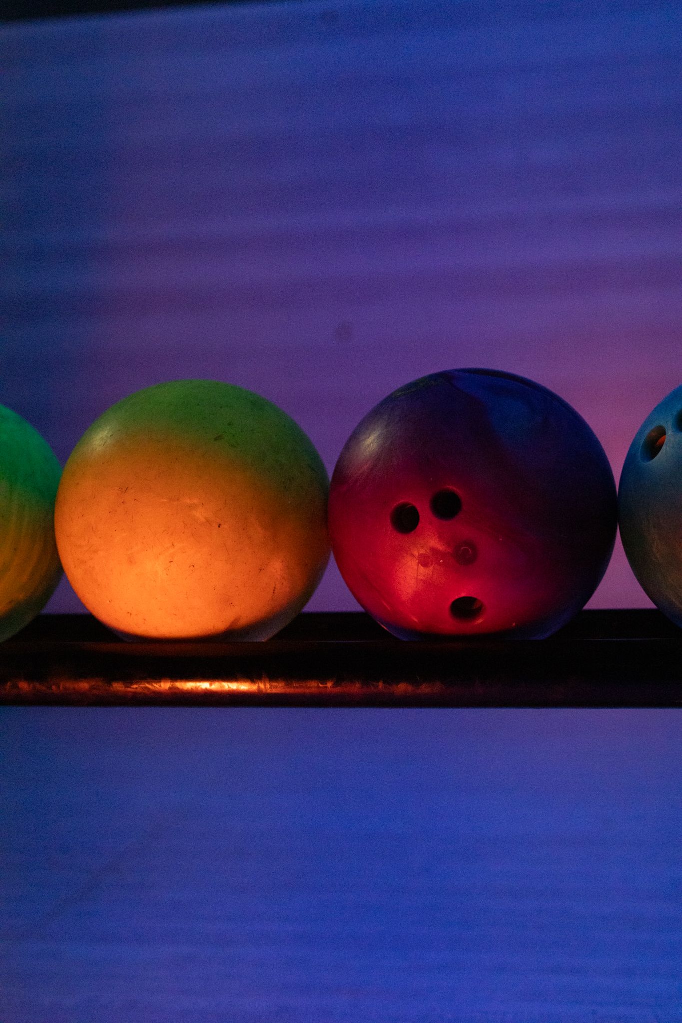 Colorful bowling balls glowing under neon UV black light on a rack in a bowling alley lane.
Yip's Hengelo - Bowlen - Brandingshoot