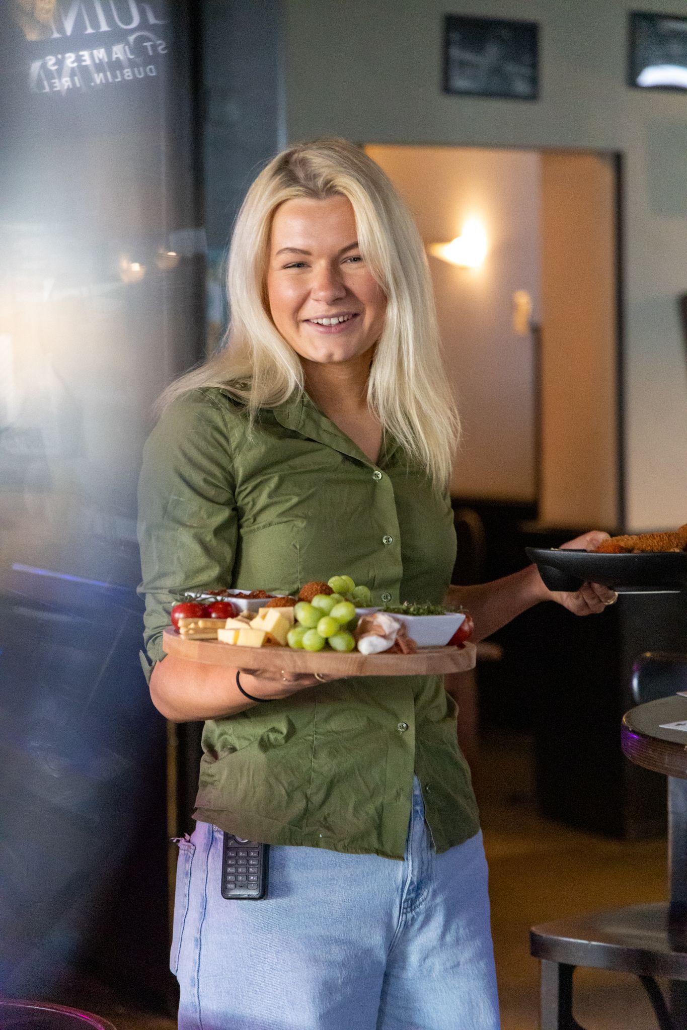 Smiling blonde waitress in green shirt carrying food platters with fruit and cheese board in a restaurant.
Yip's Hengelo - Brandingshoot