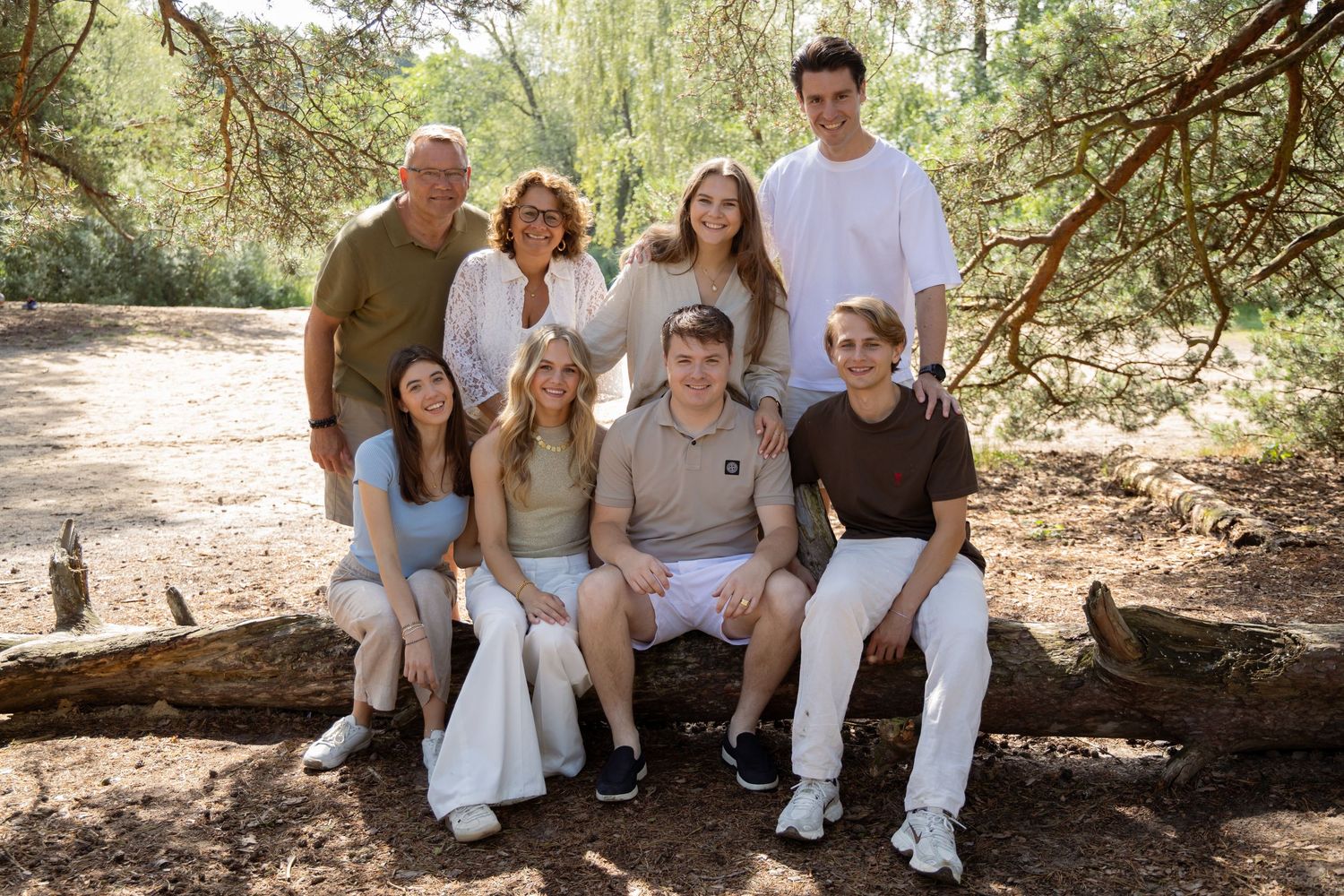 A multigenerational family of eight poses together outdoors on a log surrounded by lush green trees.
Familie Wormgoor - Familieshoot