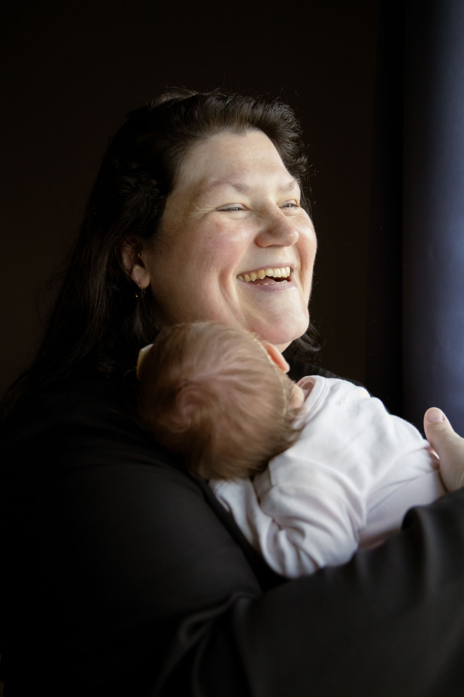 Joyful dark-haired mother laughing while holding newborn baby close to her chest.
Ellis - Newborn shoot