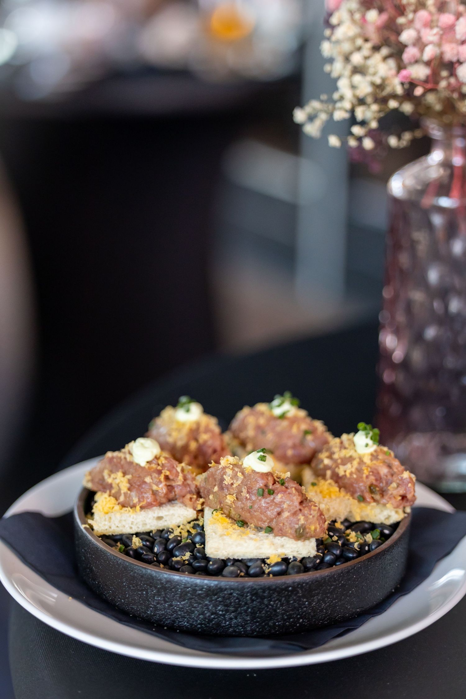 Elegant appetizers on toasted bread topped with seasoned meat and cream, served in a dark ceramic dish.