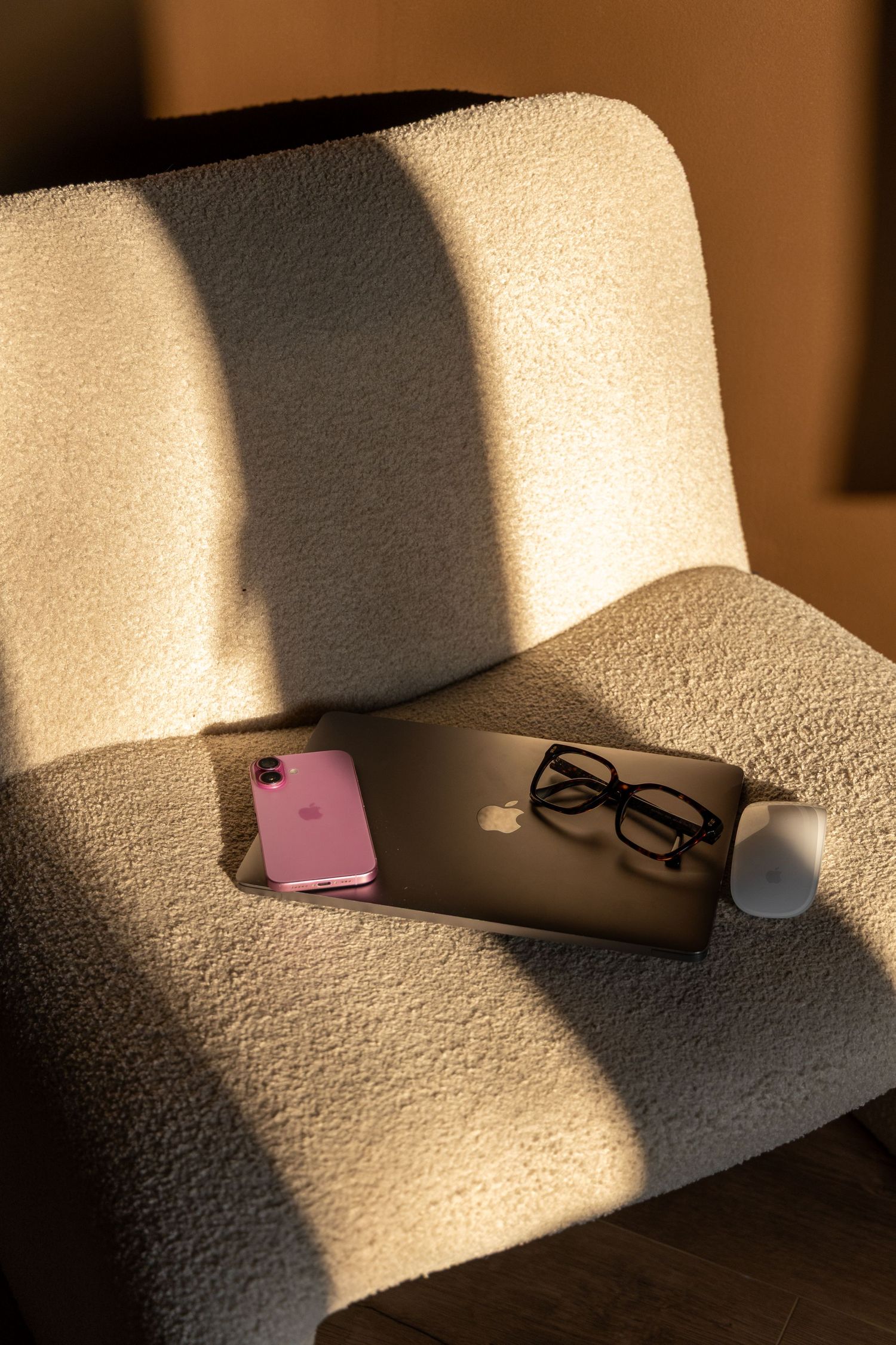 Pink iPhone and glasses rest on a laptop atop a cozy white boucle armchair in warm sunlight.
Emma - Reefolution - Brandingshoot