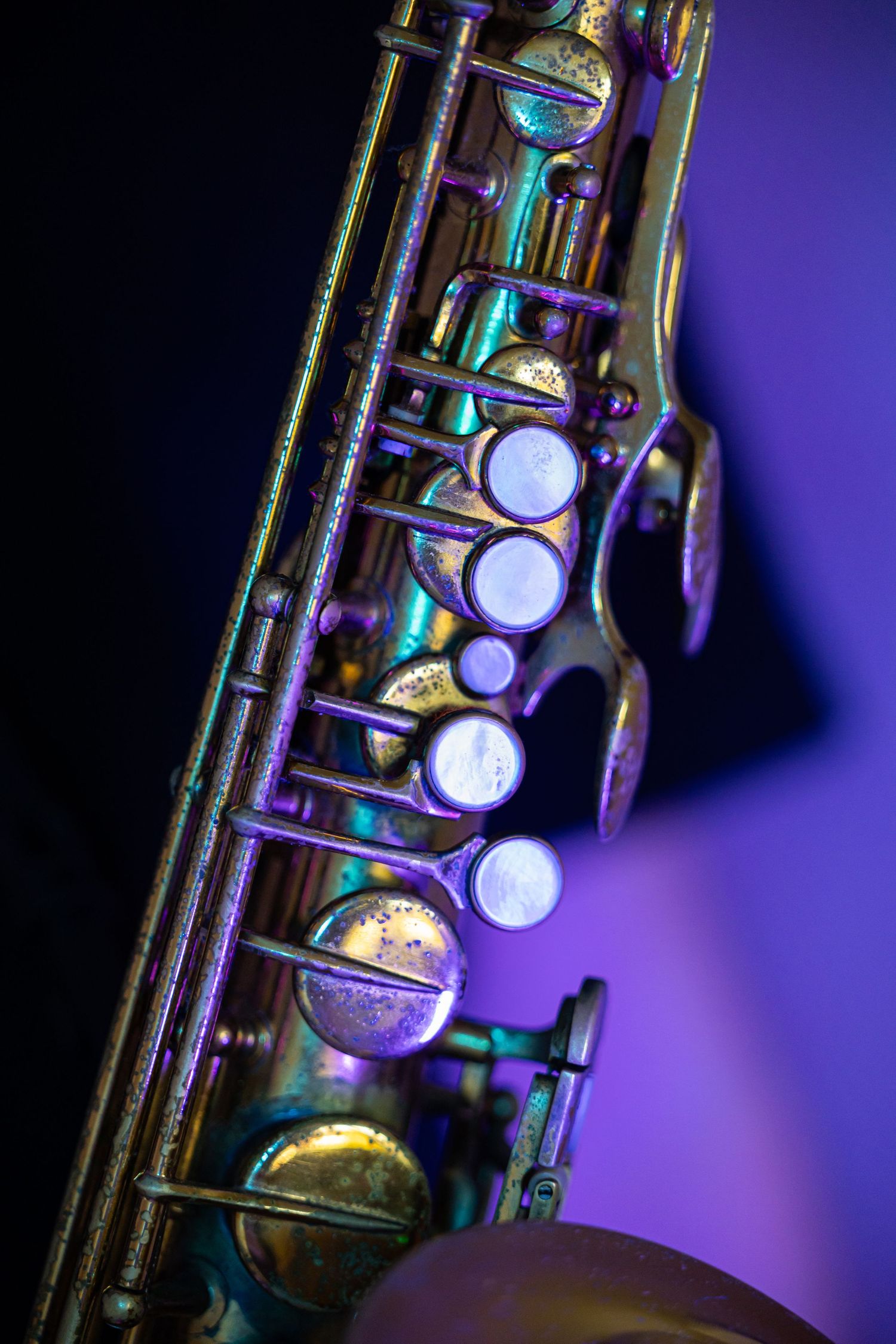 Close-up of a vintage saxophone with colorful purple and teal lighting highlighting its brass keys and intricate mechanisms.