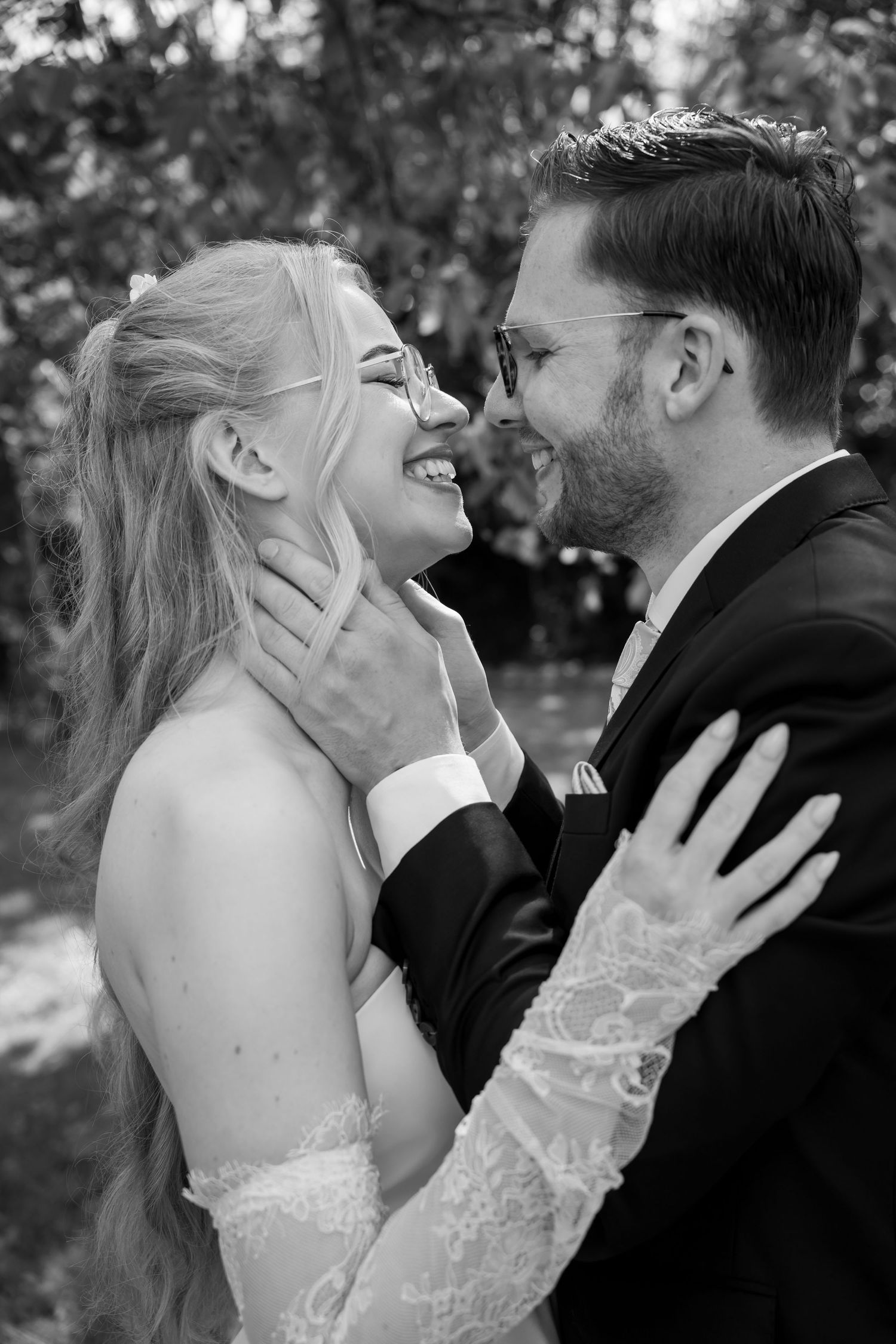 Black and white photo of a laughing bride and groom sharing a tender moment, with the groom gently holding her face.