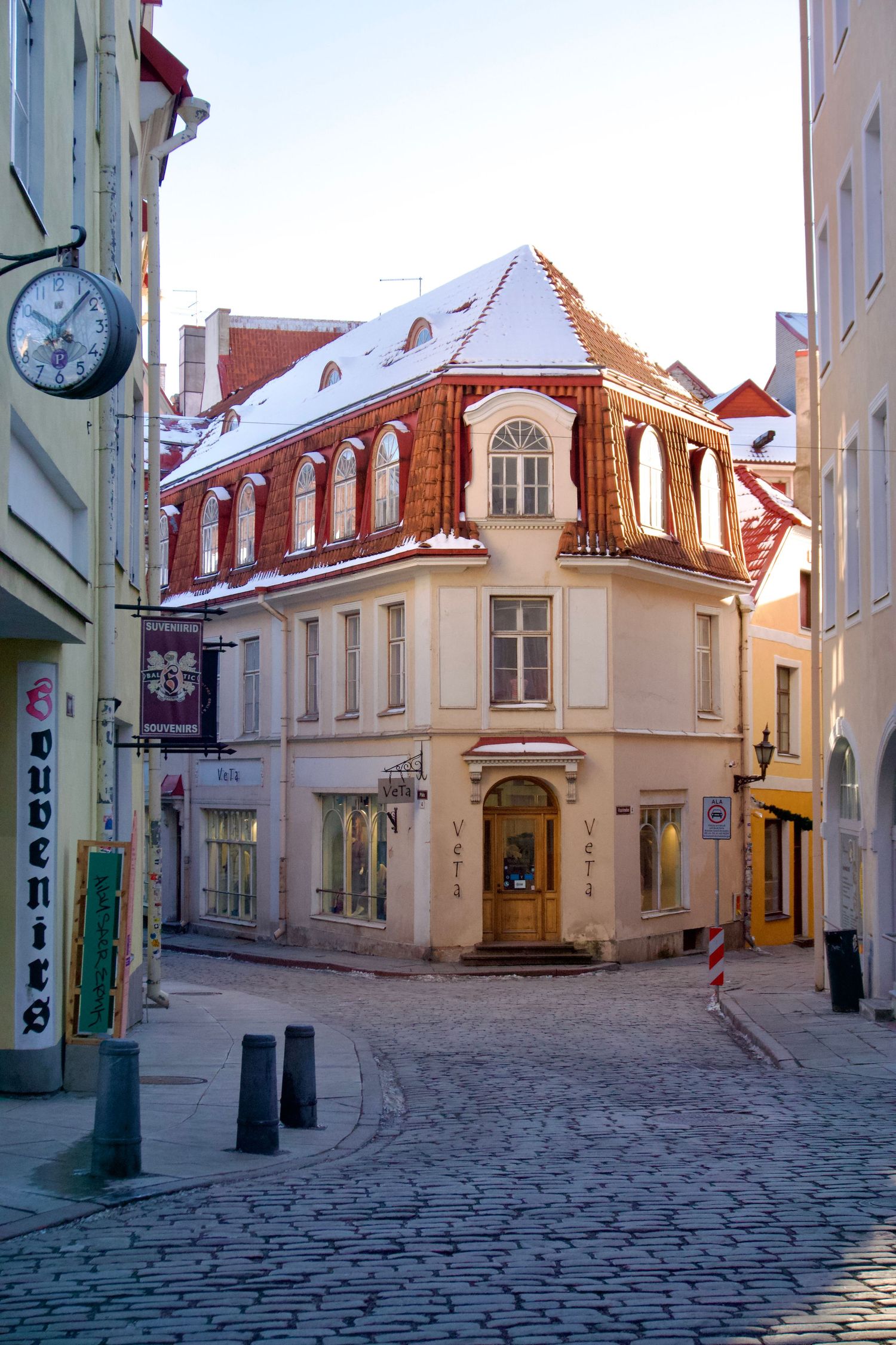 Snow-dusted historic building on a cobblestone street corner in Tallinn's old town, featuring ornate red roof architecture.
Lynn - Tallinn