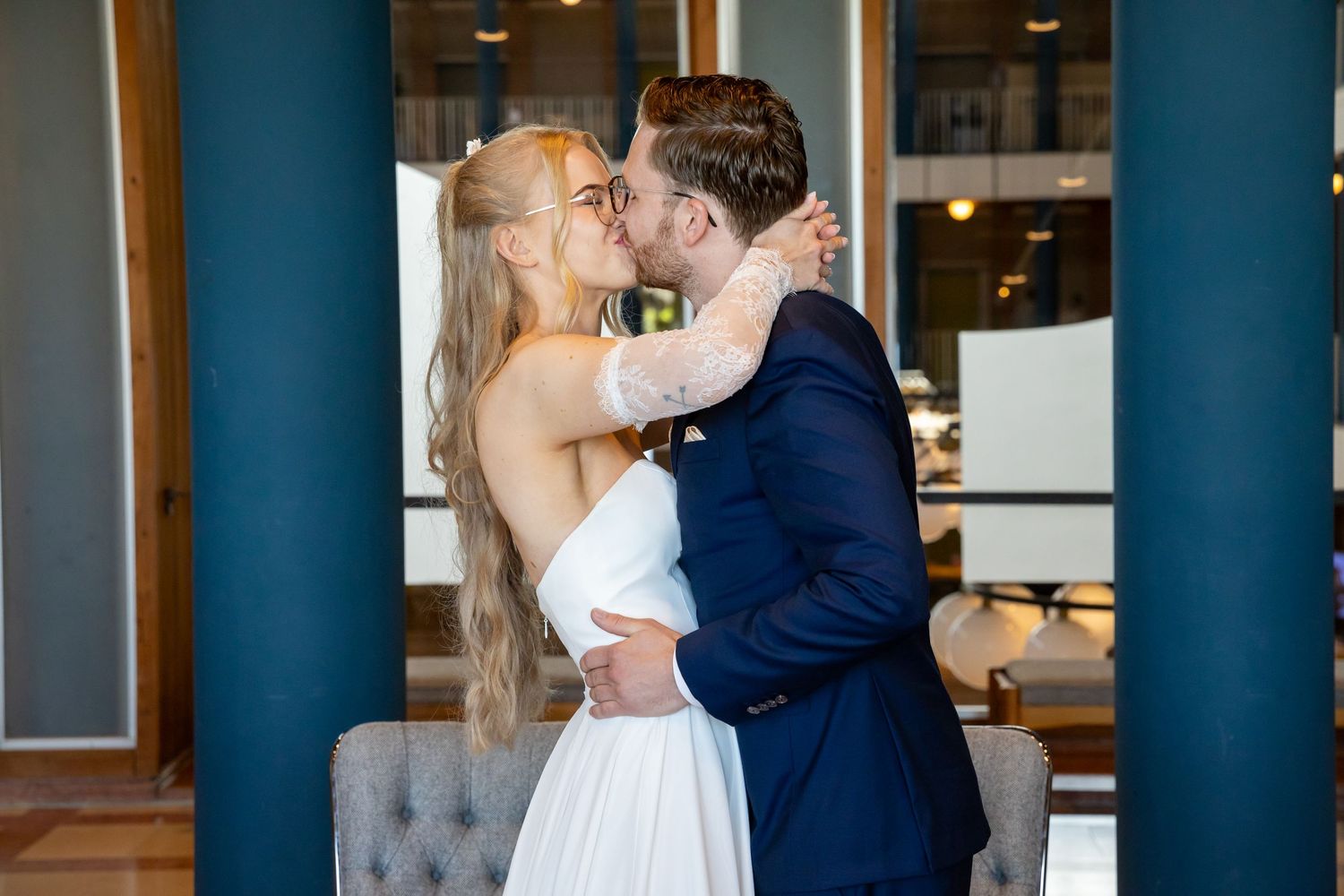Bride and groom sharing a romantic kiss at their wedding venue, bride in white gown, groom in navy suit.