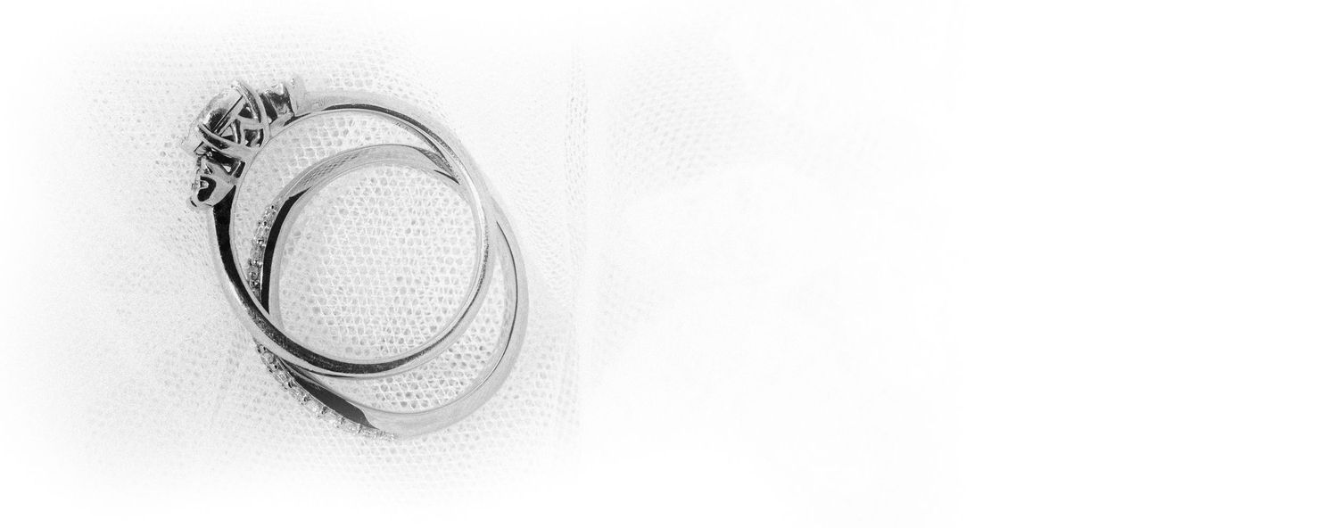 Close-up black and white image of elegant wedding rings on a textured white background.