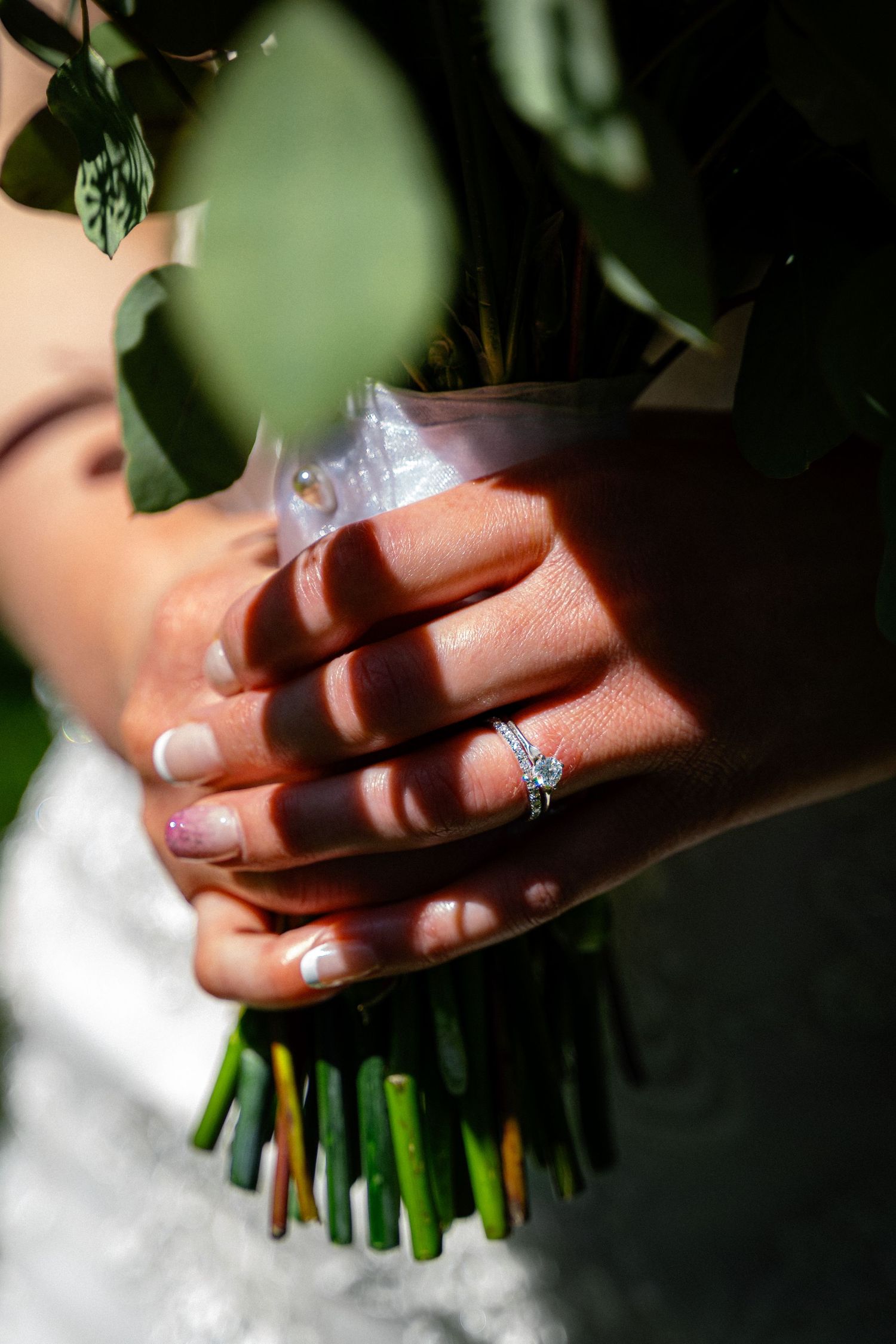 Close-up of bride's hand with diamond engagement ring holding a lush green wedding bouquet.