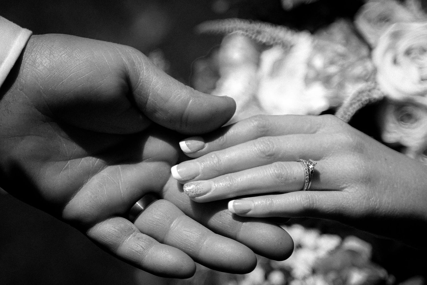 Black and white photo of a groom placing a wedding ring on the bride's finger during the ceremony.