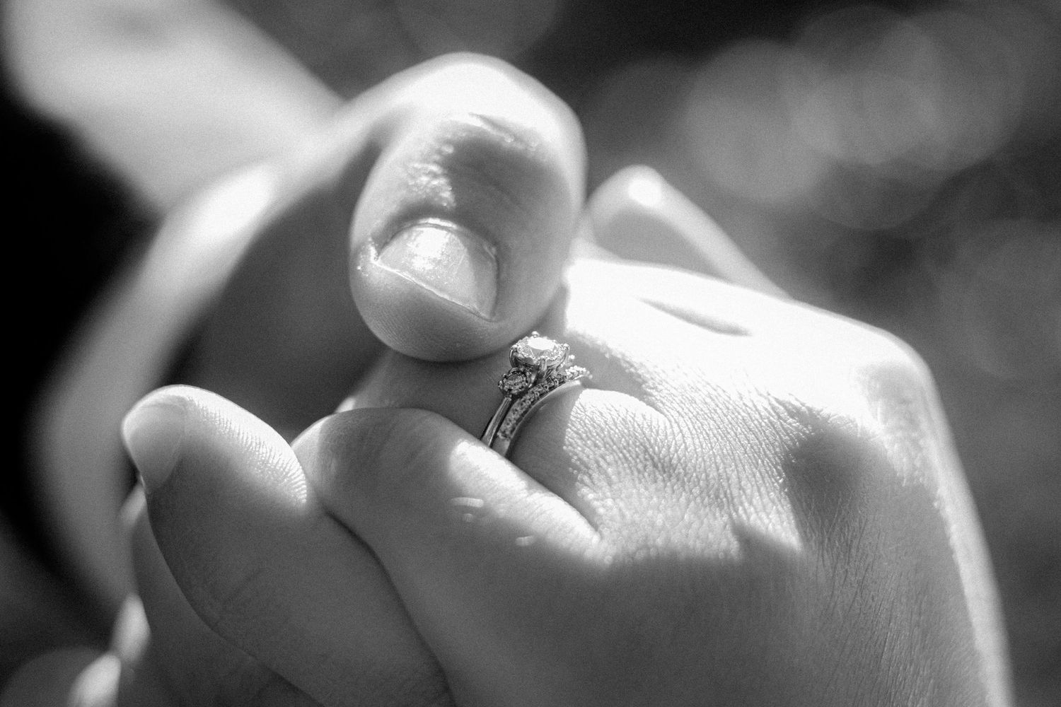 Close-up black and white photo of a couple holding hands showing an engagement ring.